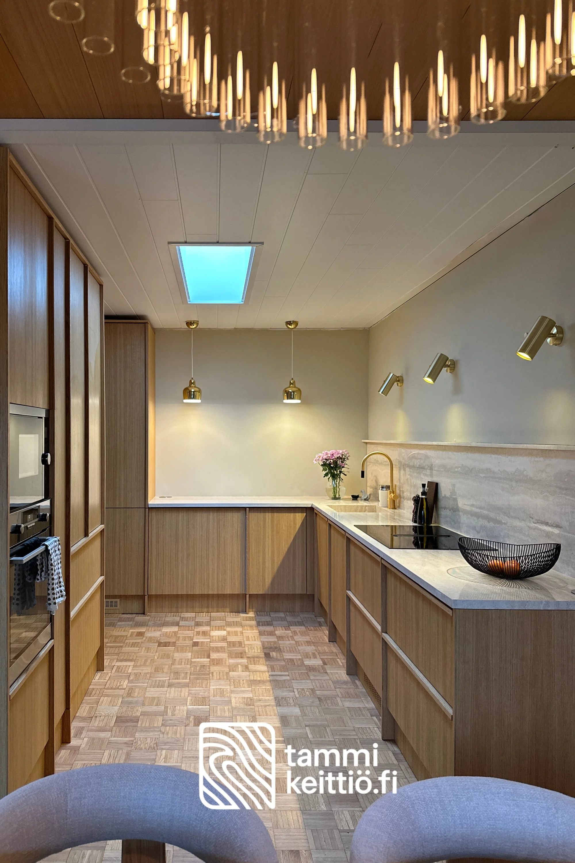 Yläkaapiton tammikeittiö travertiinitasolla ja kivihyllyllä messinkiseinälampuilla