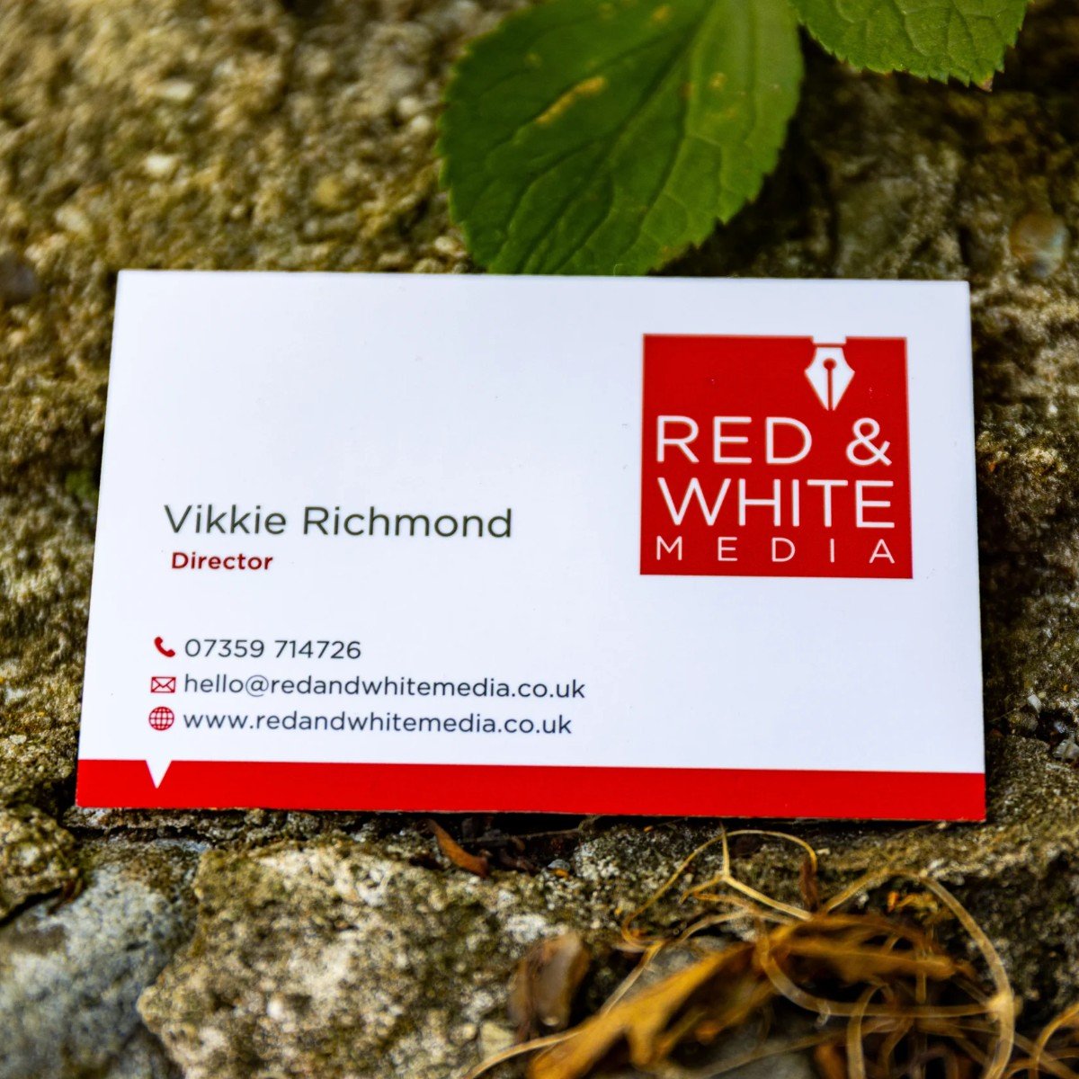 Business card placed on the ground with a clear logo of Red & White Media, containing contact information for Vikkie Richmond, the director, including phone number, email, and website.