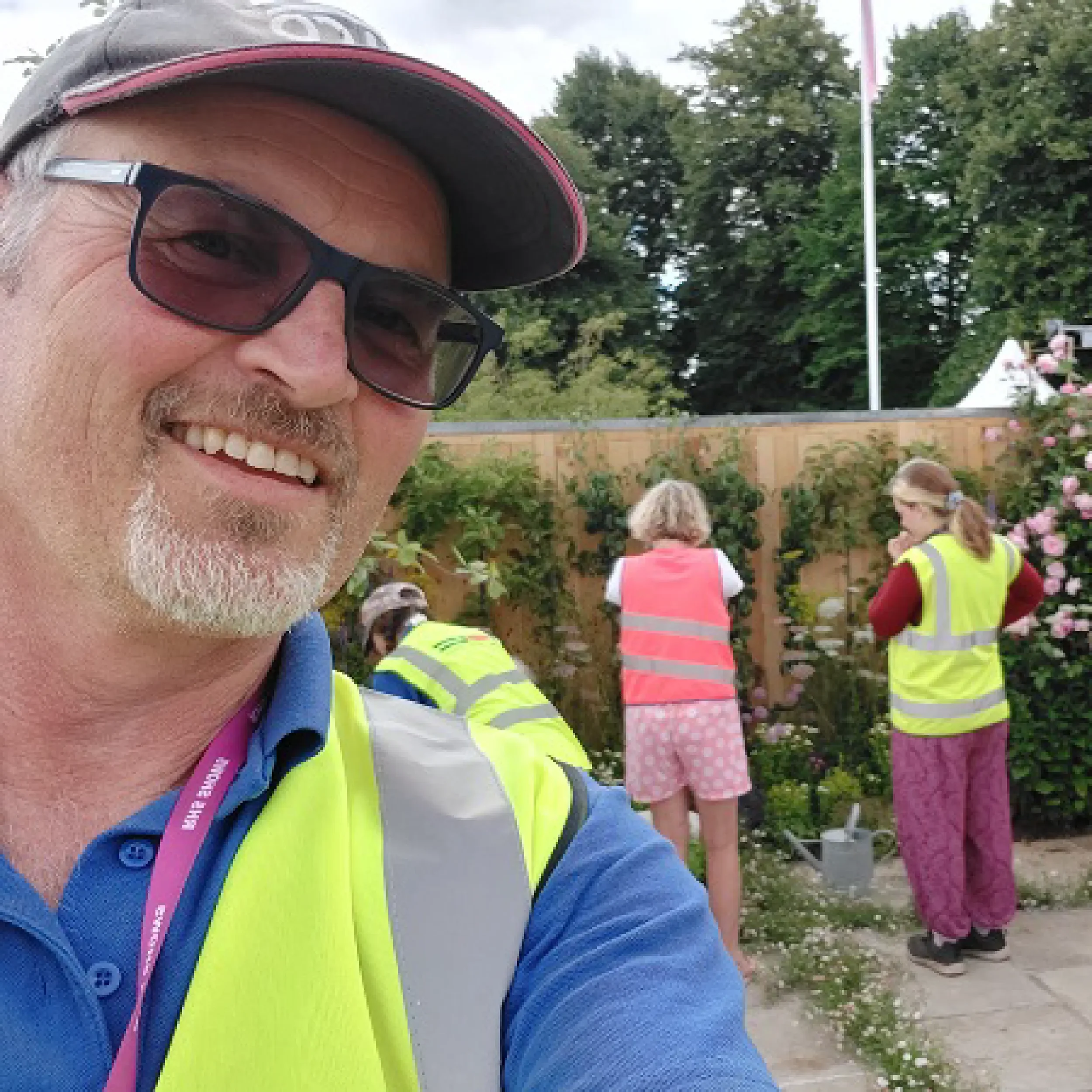 Andy Woodason, owner of Bowood Landscapes LTs is wearing sunglasses, a cap and a high-vis vest. He is looin gat the camera and smiling. Two women in high-vis vests can be seen in the background
