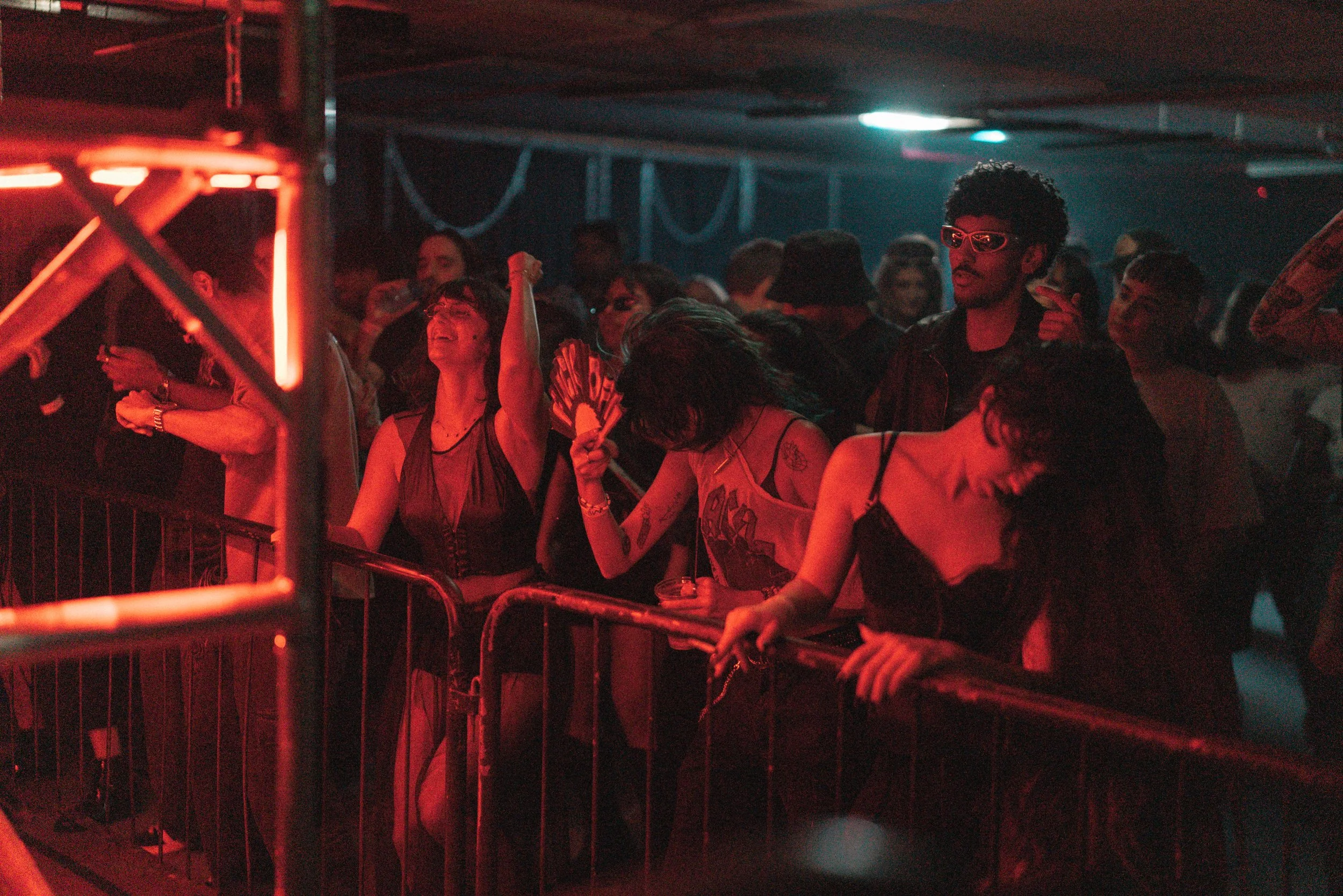 People dancing and enjoying a concert in a dark indoor music venue with colorful lighting.