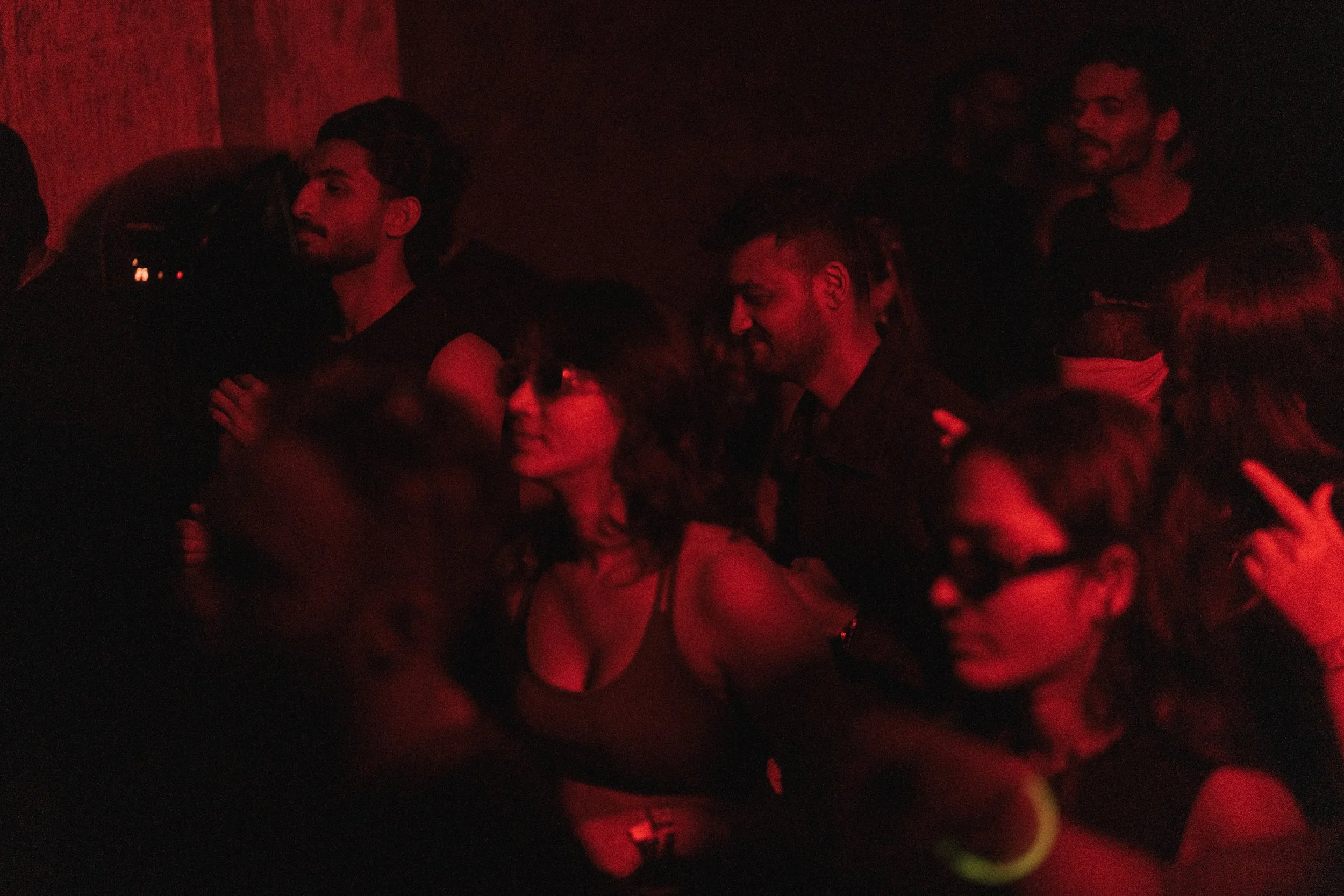 Crowd of people dancing and socializing in a dimly lit nightclub with red lighting.