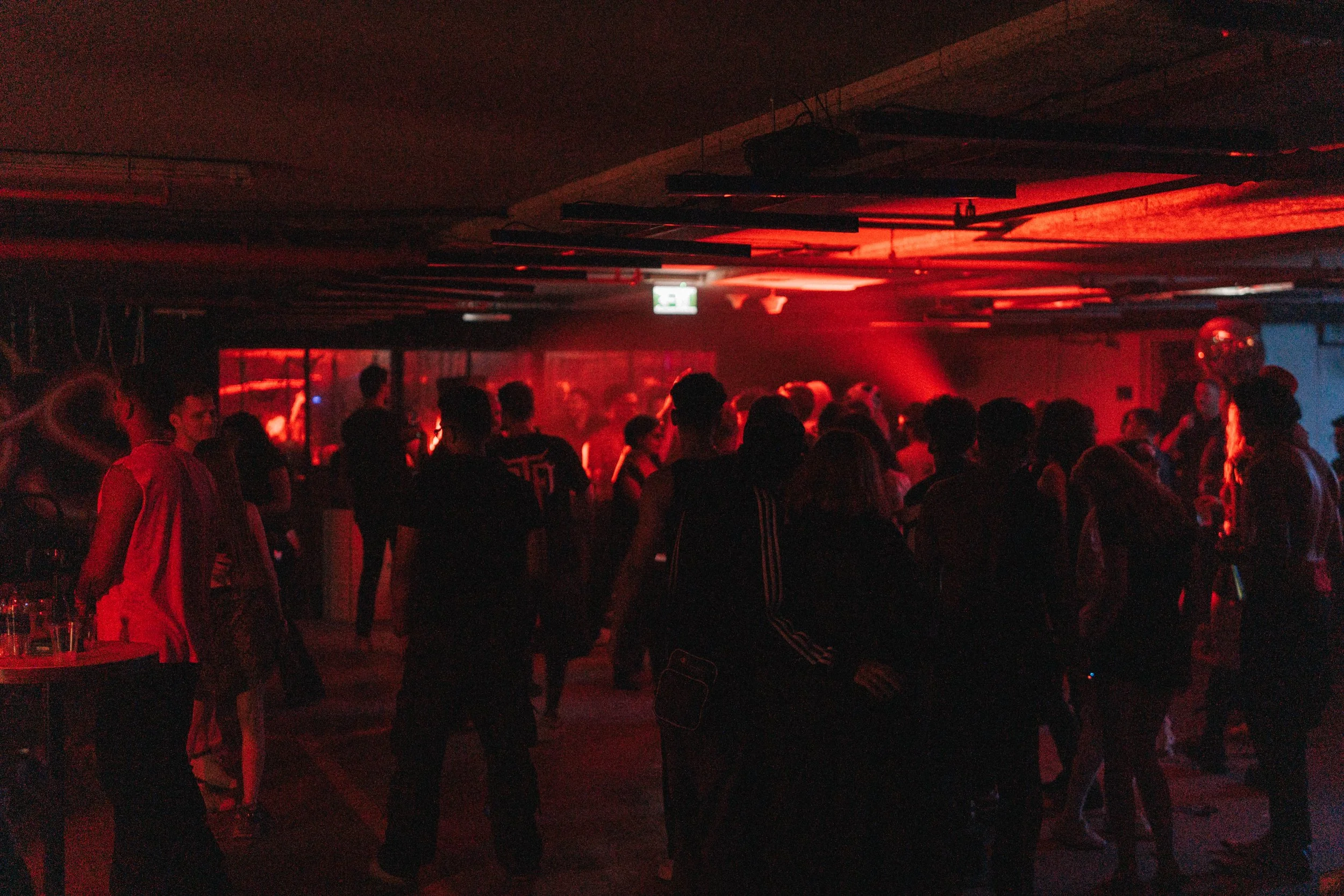 People dancing and socializing in a dimly lit nightclub with red light effects.