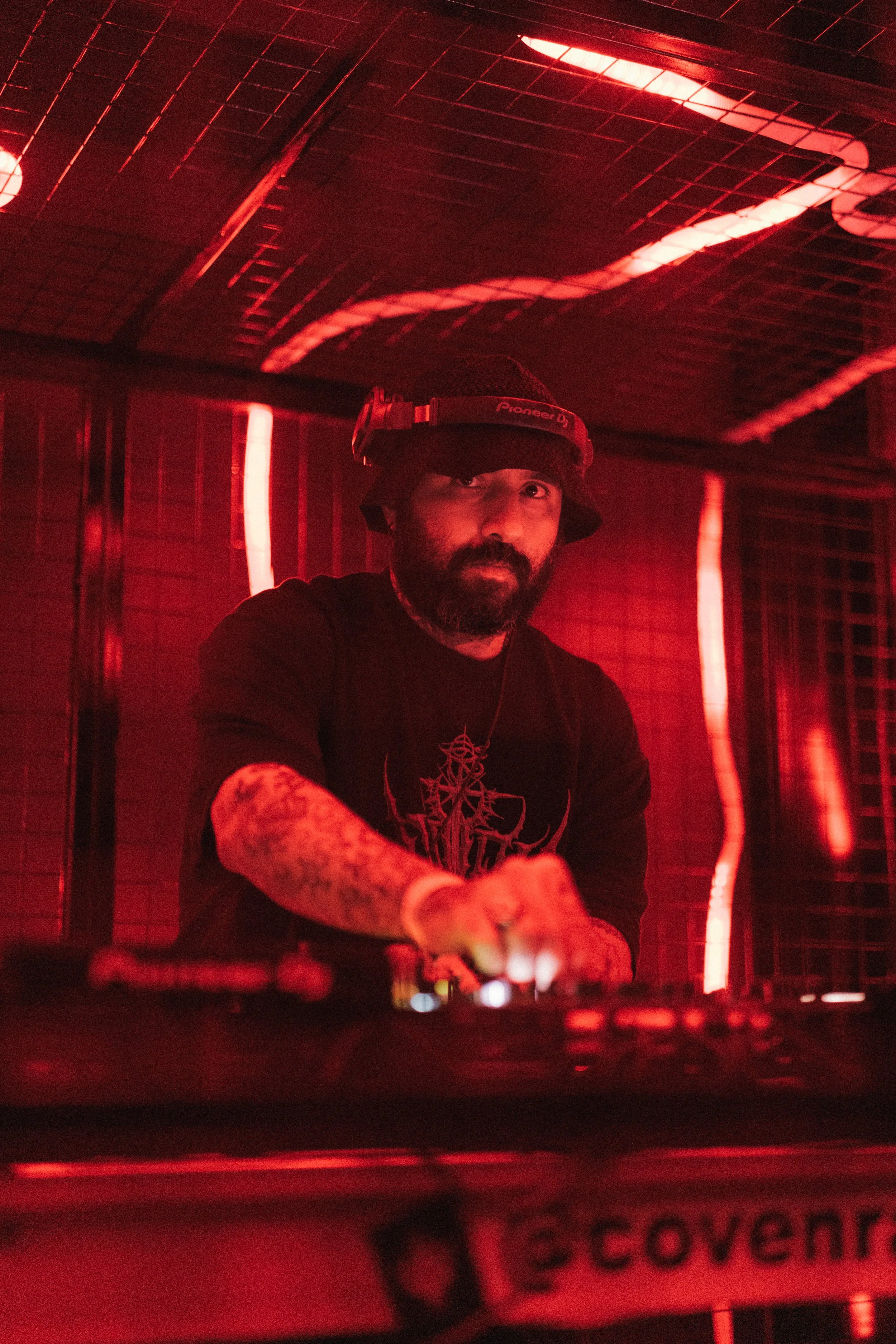 DJ mixing music at a nightclub with red lighting and wooden ceiling panels.