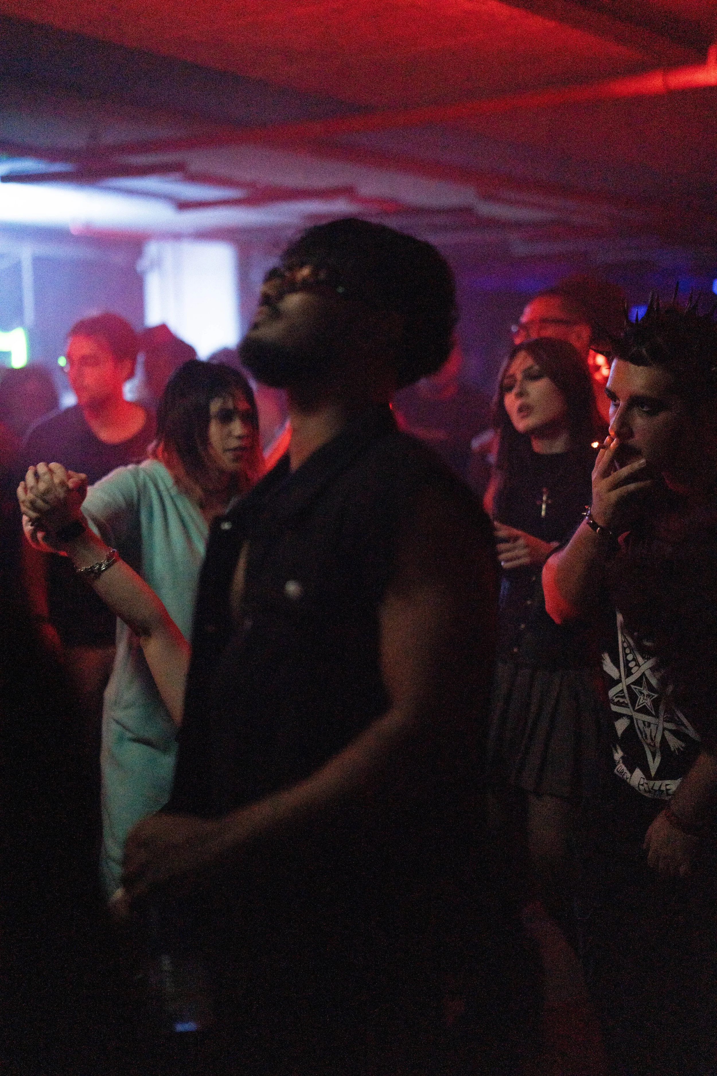 A group of people dancing and socializing in a dimly lit nightclub with colorful lights.