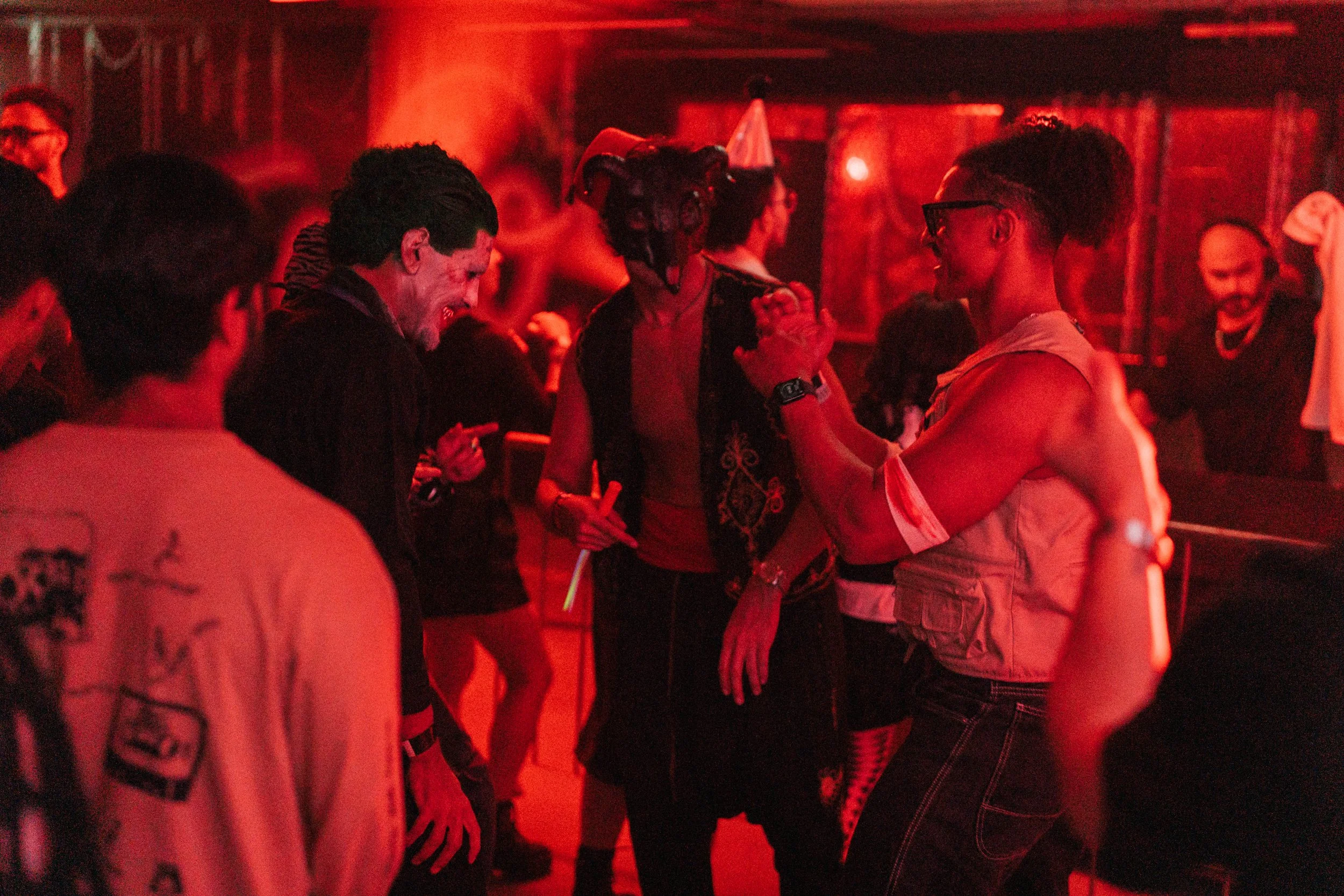 People dancing and socializing in a dimly lit club or party scene with red lighting.