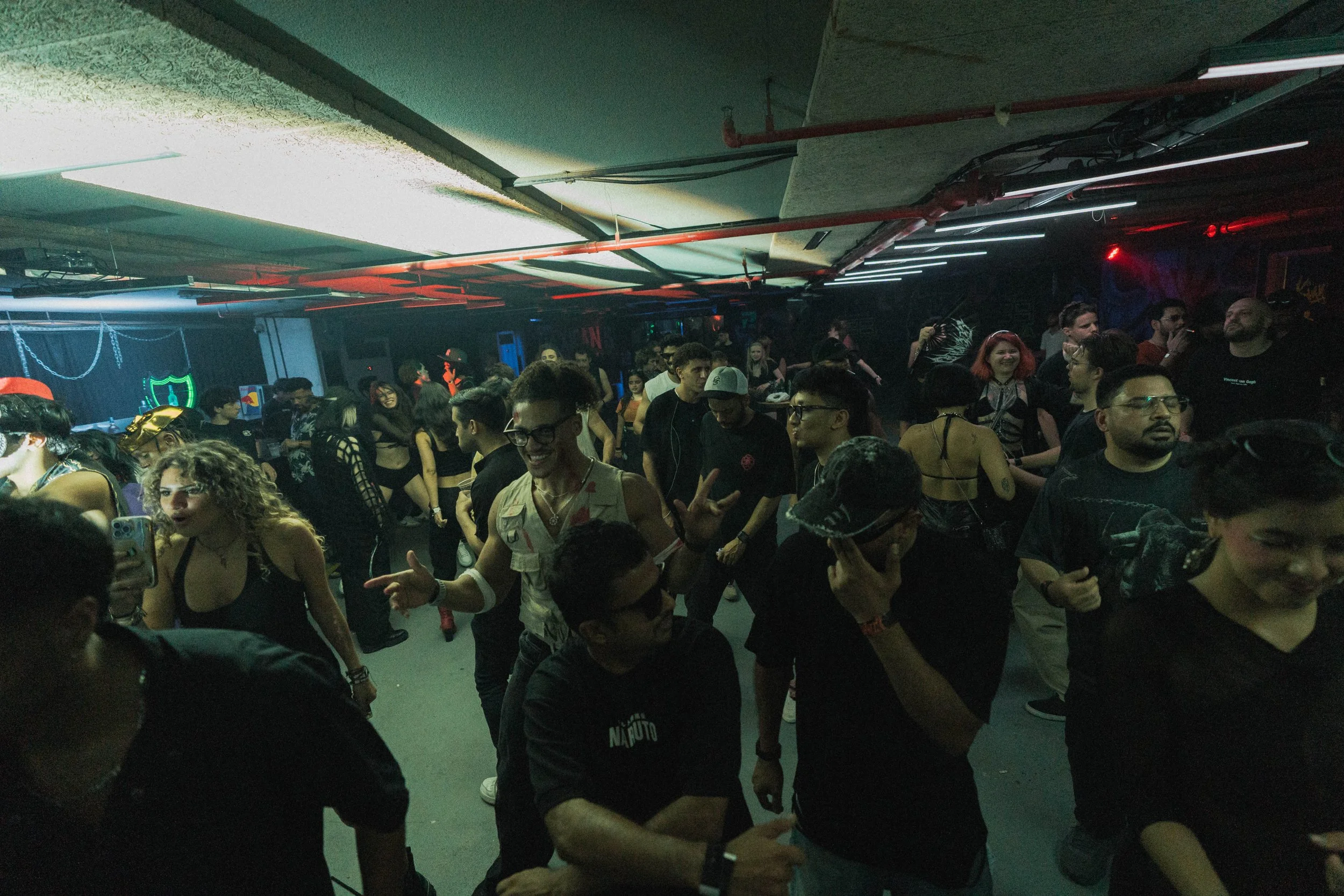 Crowd of people dancing and socializing in a dark, neon-lit nightclub or party venue.