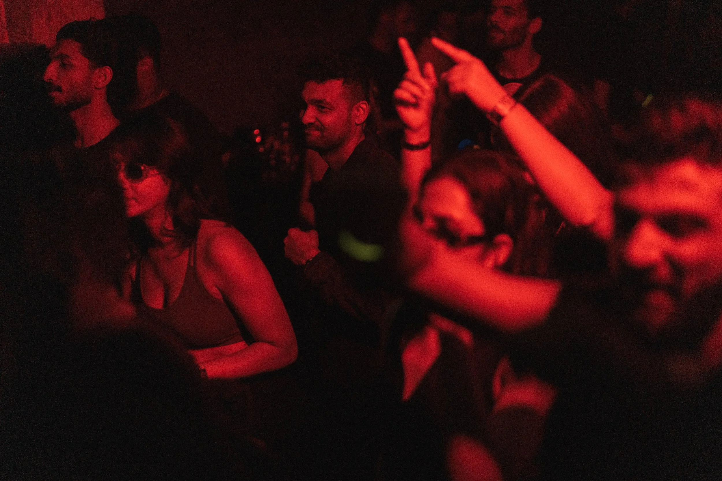 People at a concert or club, illuminated by red light, some are dancing and enjoying music.