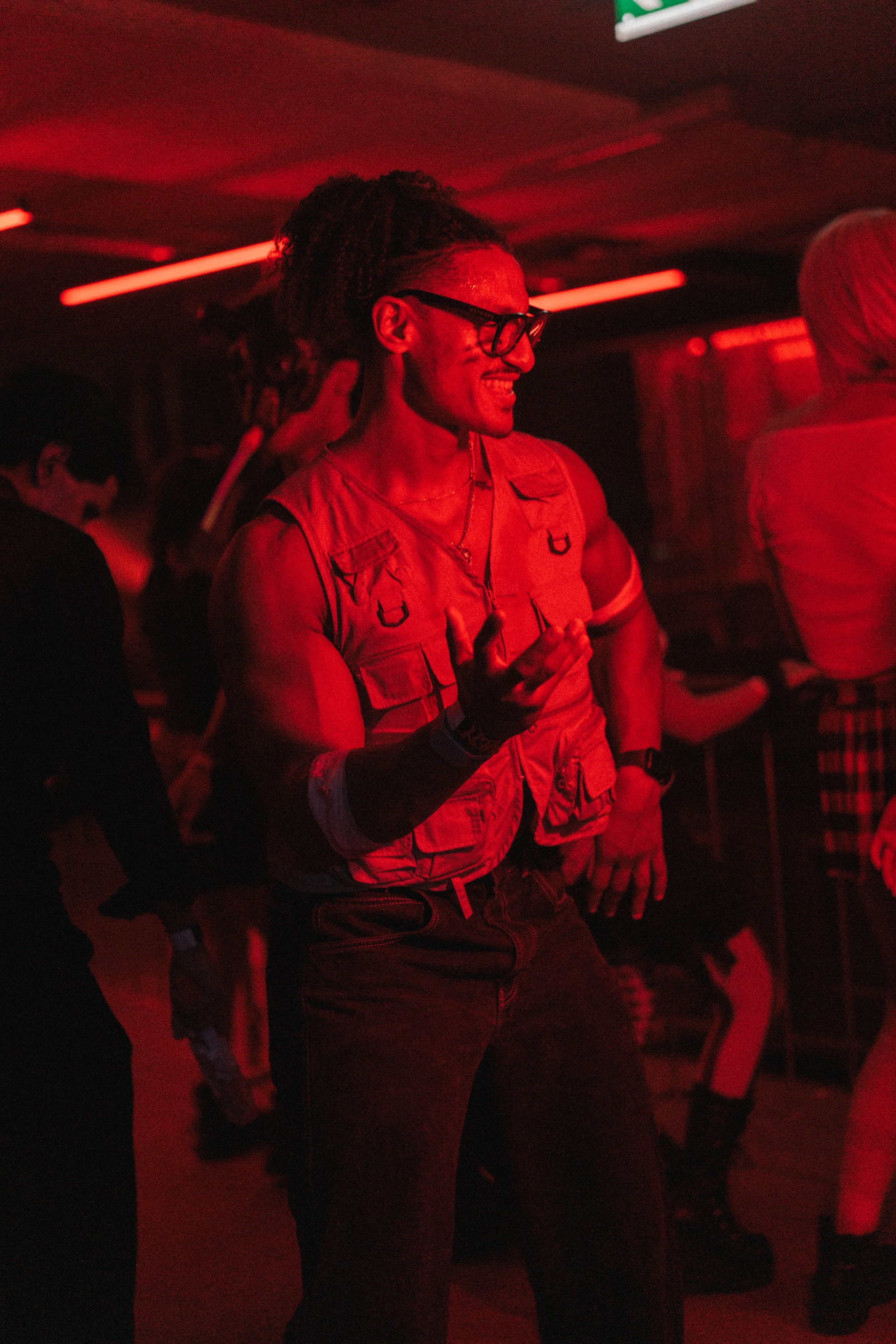 A person with curly hair and glasses dancing in a dimly lit, red-lit room.