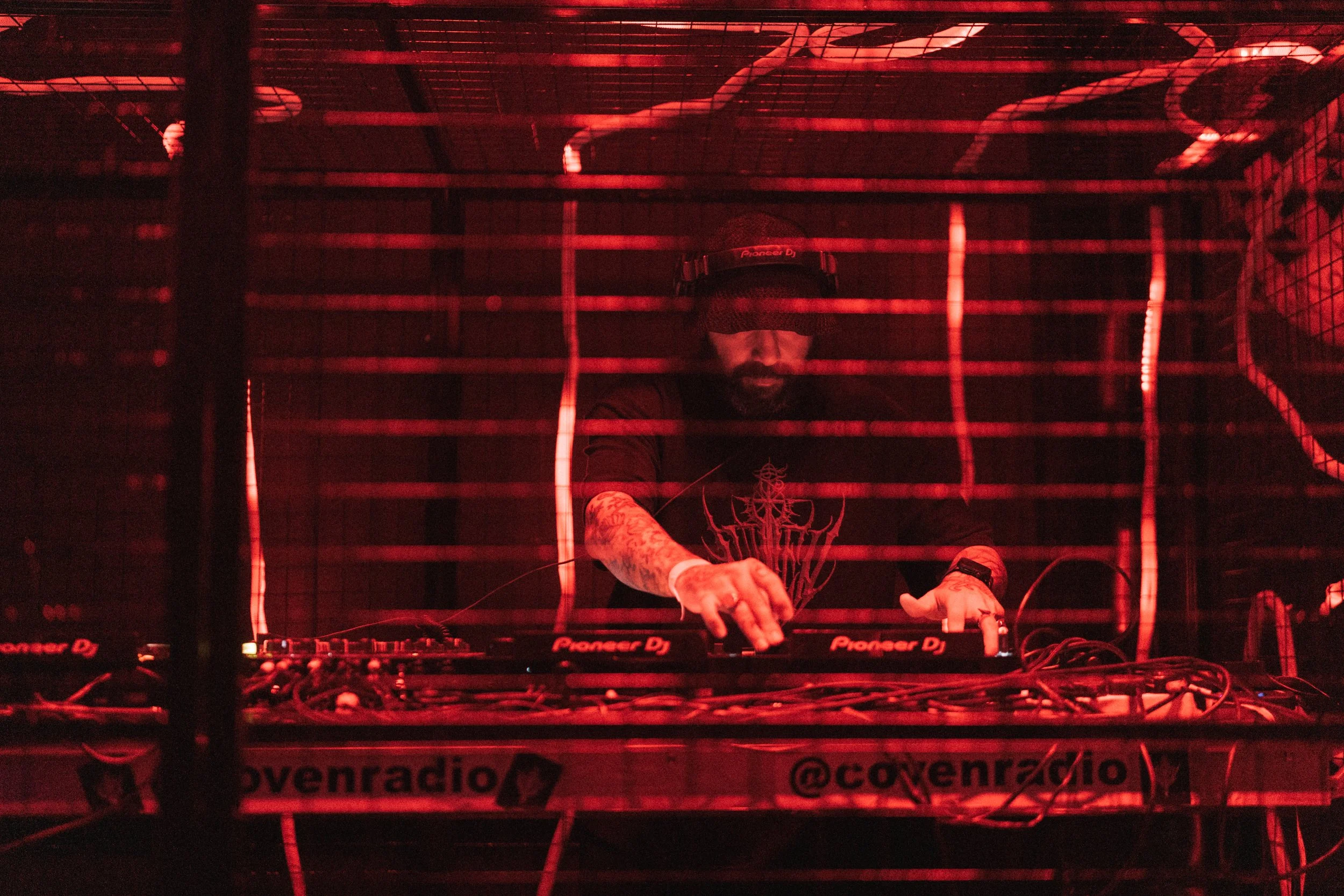 DJ performing behind a red lighting grid at a nightclub