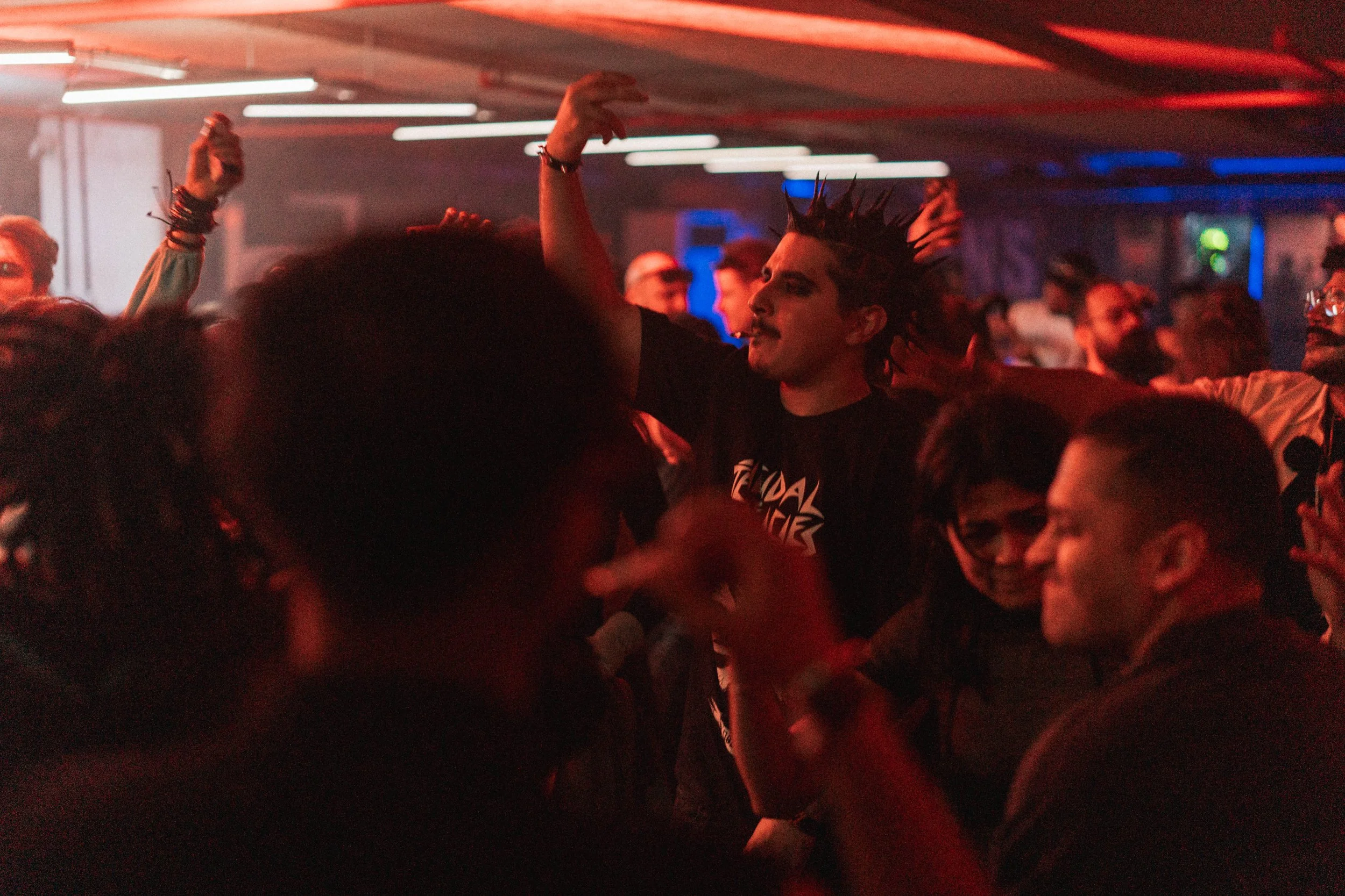 People dancing and having fun at a crowded concert or nightclub with red and blue lighting.