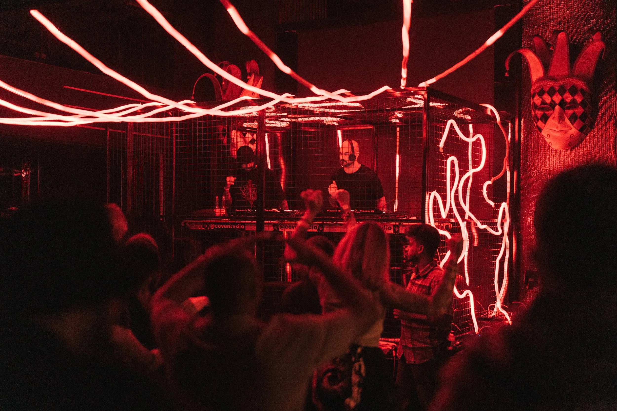 People dancing and DJ playing music in a club with red neon lighting and artwork on the walls.
