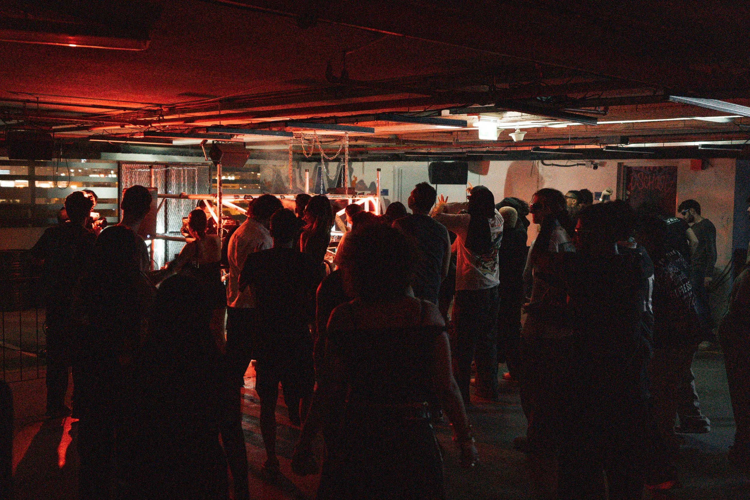 People dancing and socializing in a dimly lit nightclub with neon and colorful lighting.