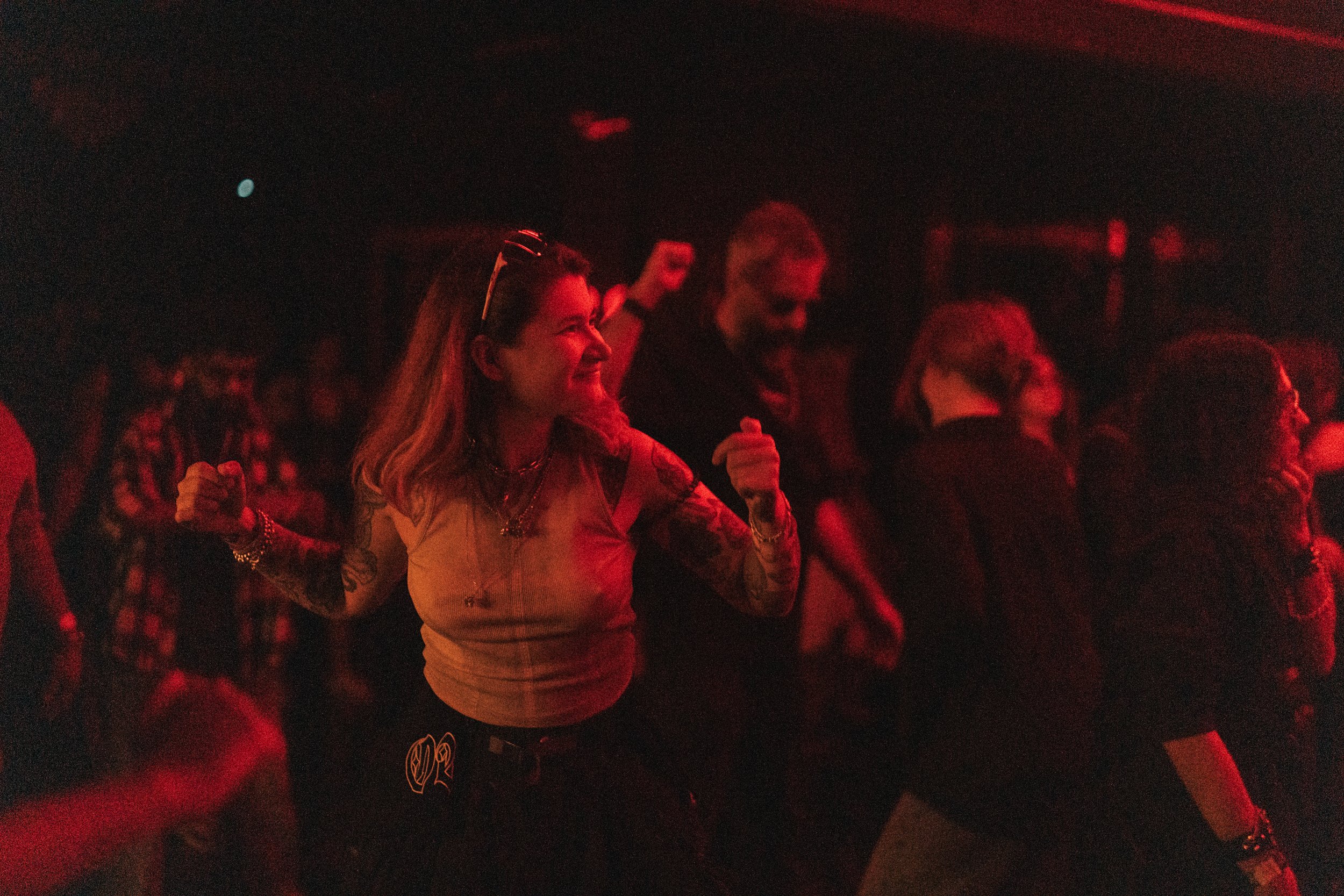 A group of people dancing and enjoying themselves in a dimly lit, red-hued environment, possibly at a concert or nightclub.