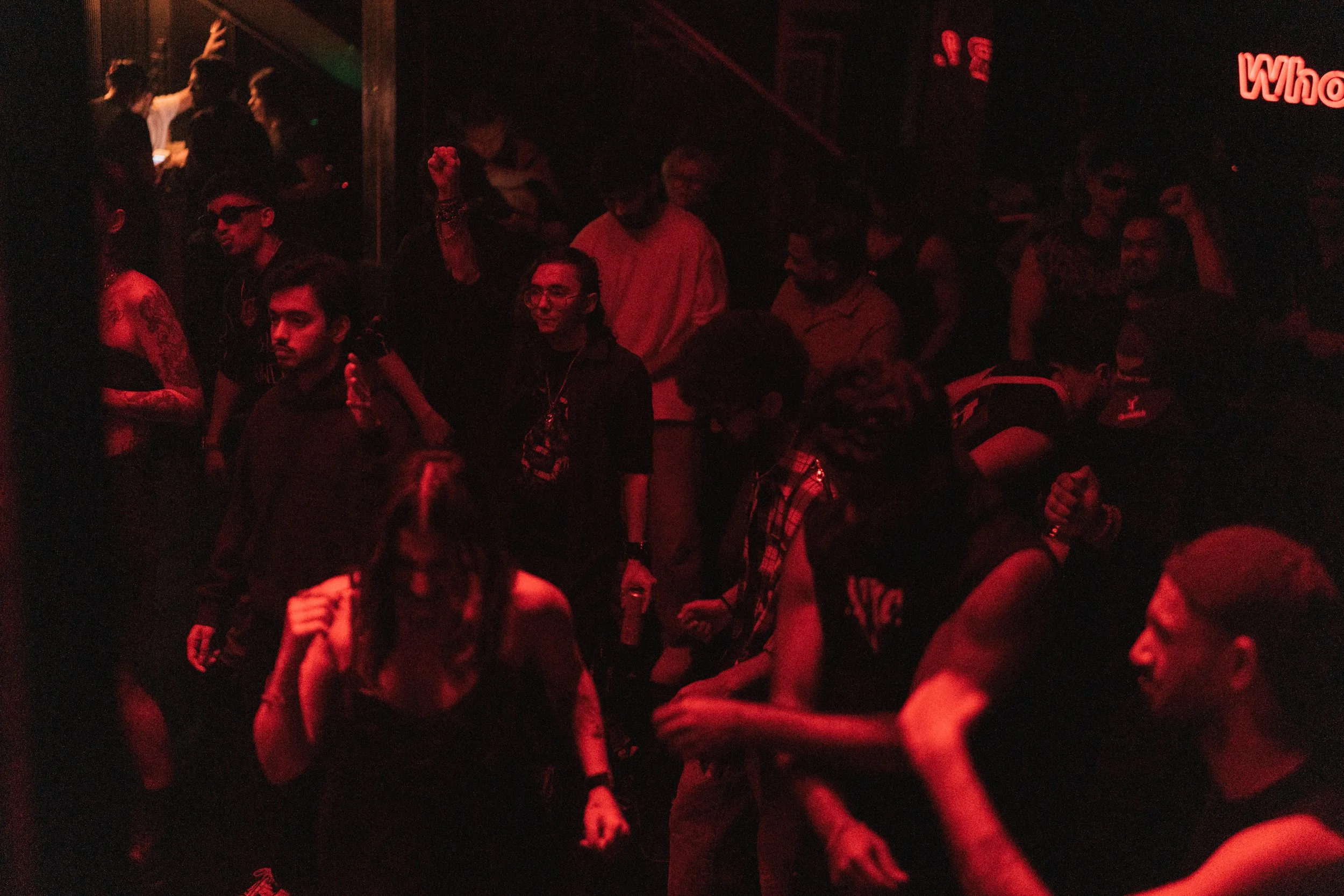 Crowd of people at a dimly lit nightclub or concert, with some dancing and others socializing.