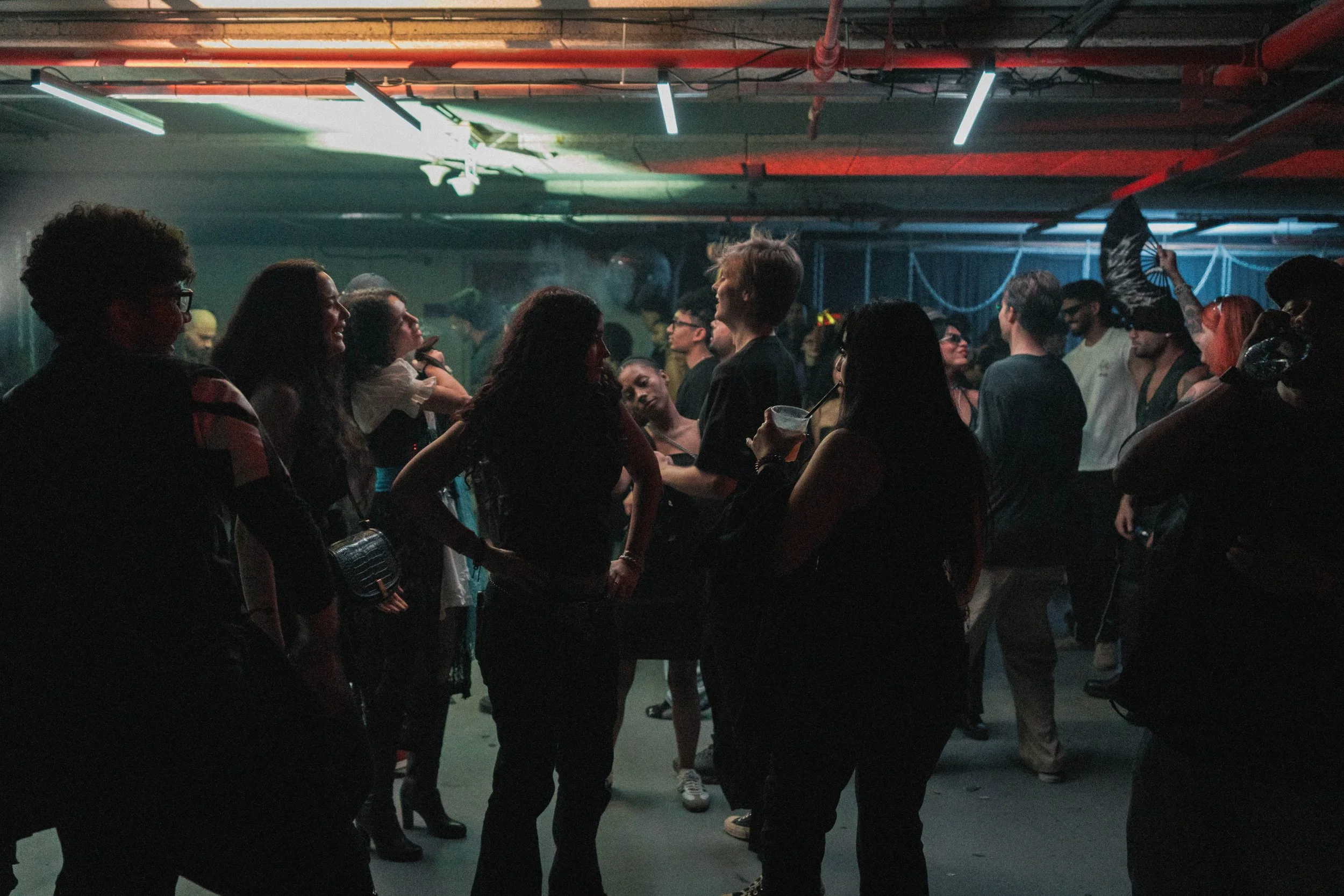 People dancing and socializing at a dimly lit indoor party or nightclub with colored neon and LED lights.