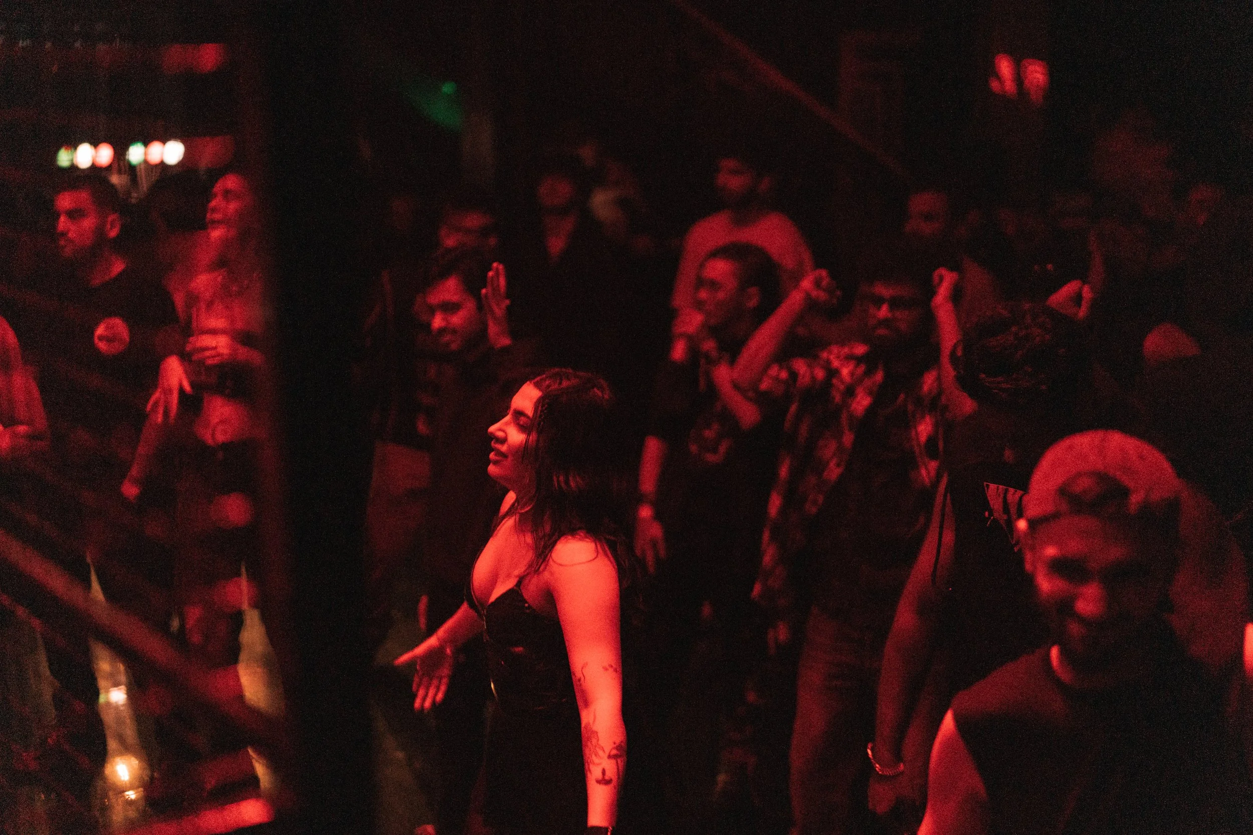 People dancing and enjoying music in a dark, red-lit nightclub or concert venue.