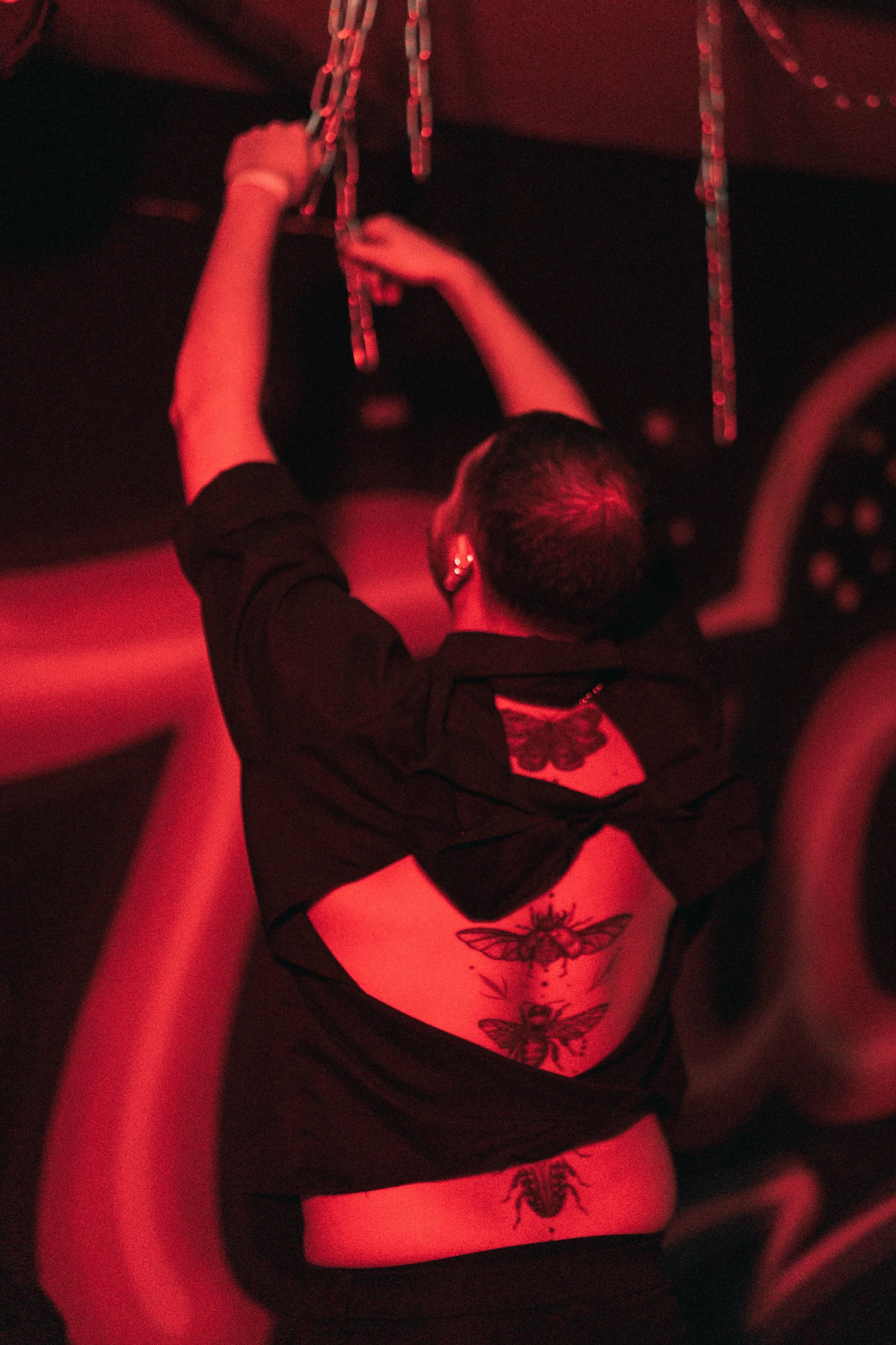 Person with tattoos on their back reaching up and hanging chains in a dimly lit room with red lighting.