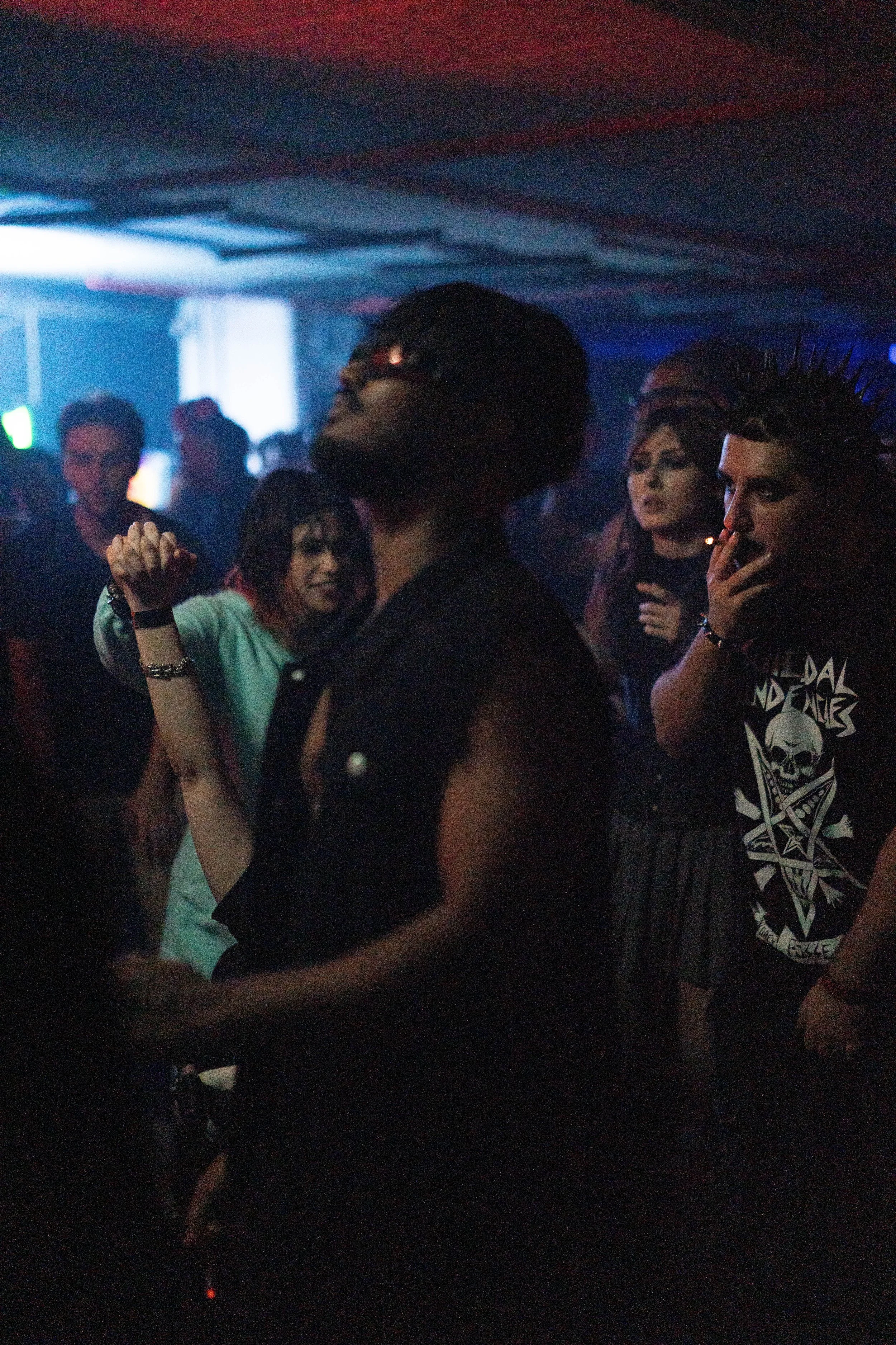 People dancing and socializing in a dark, colorful nightclub or party setting with neon lights.