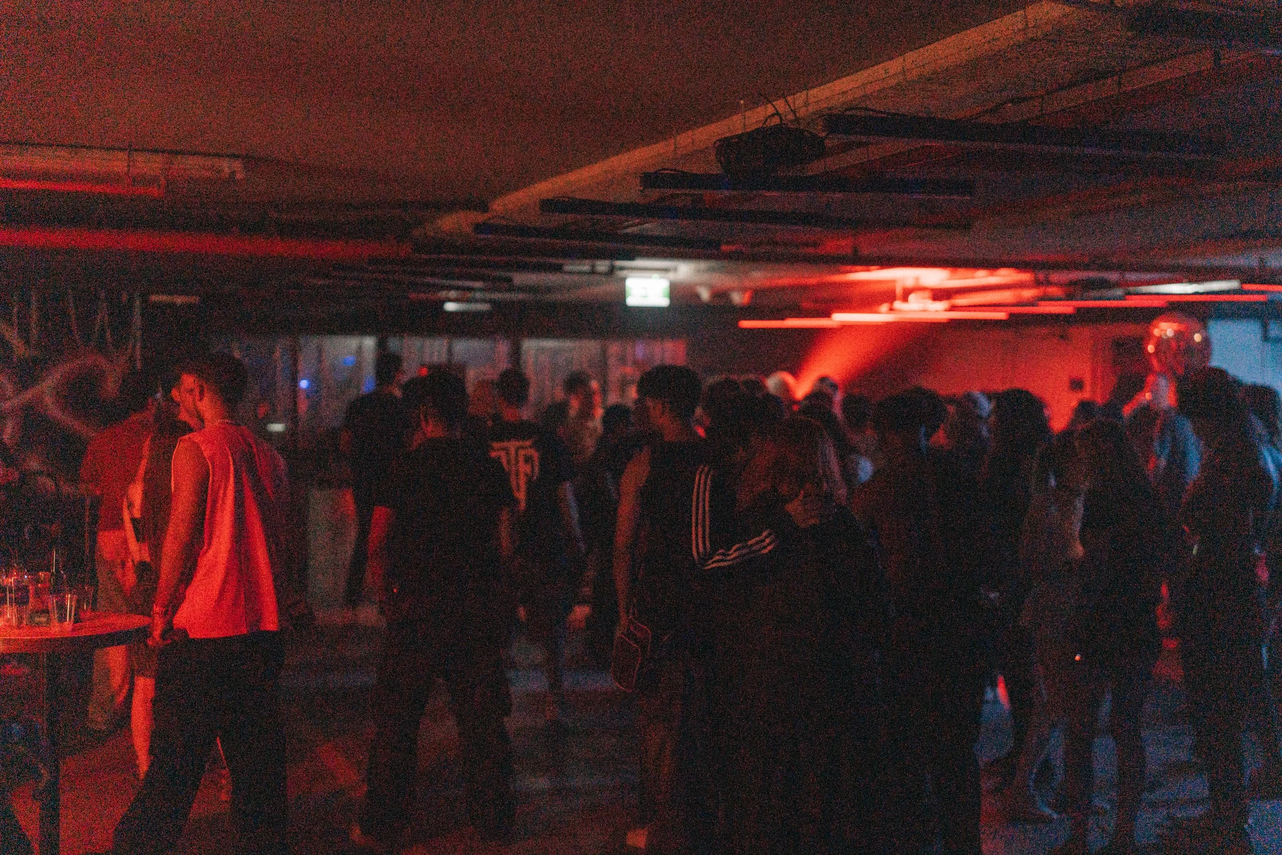People dancing and socializing in a dimly lit nightclub with red and blue lights.