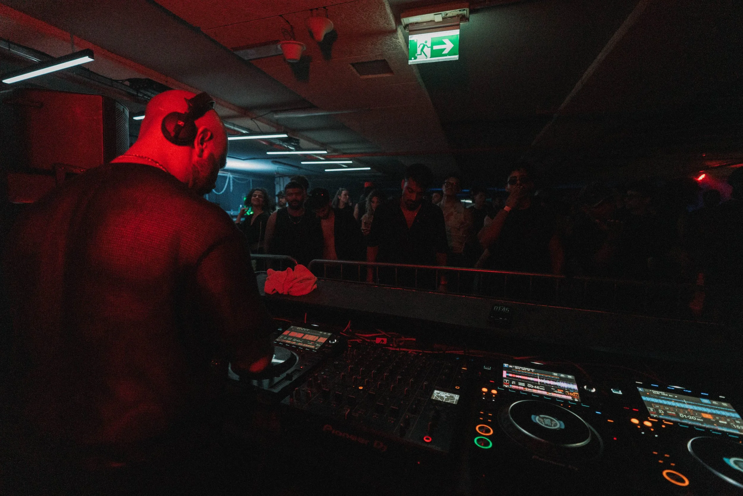 A DJ performing at a nightclub with people dancing and socializing in the background.