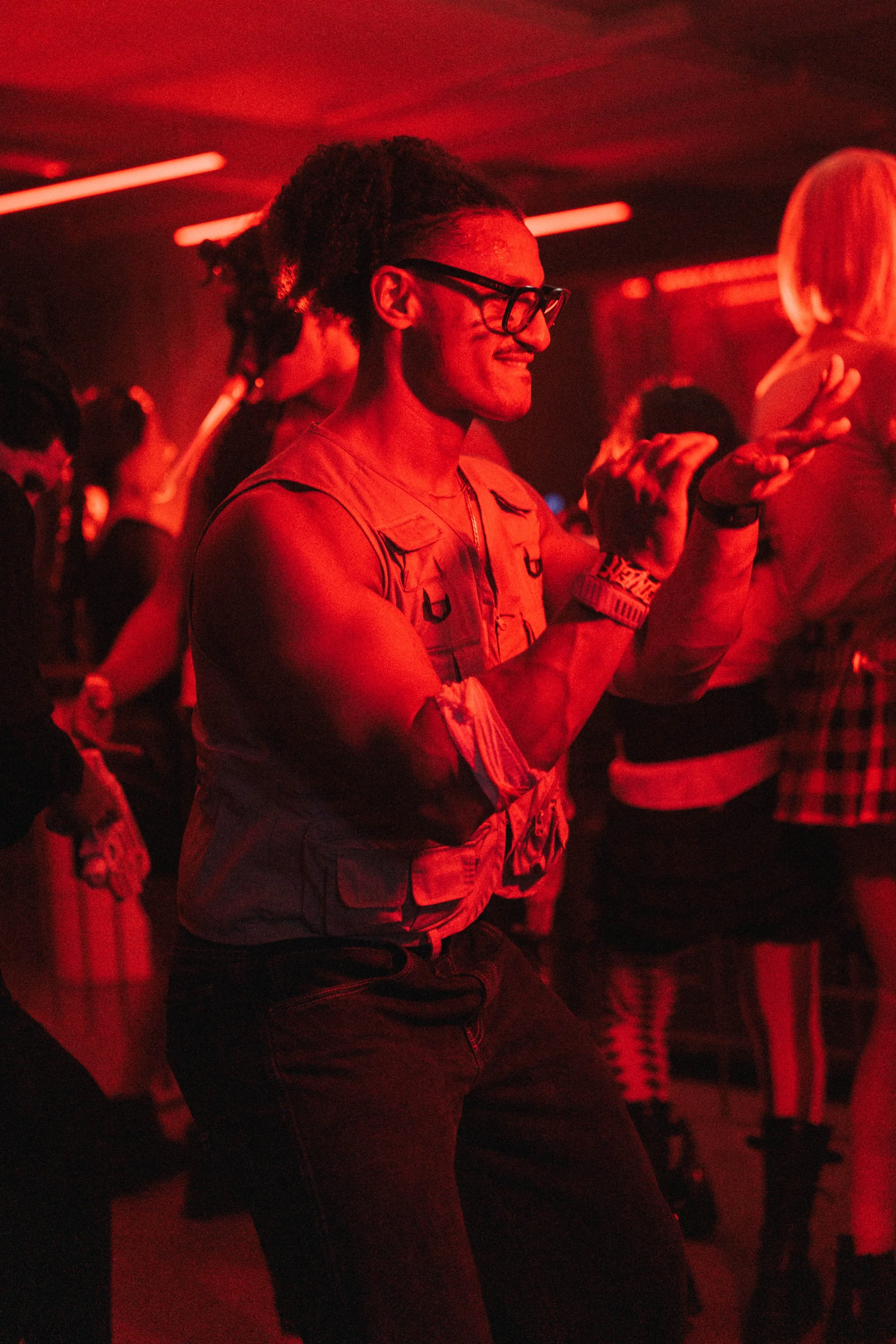 Person dancing in a red-lit nightclub with other people in the background.