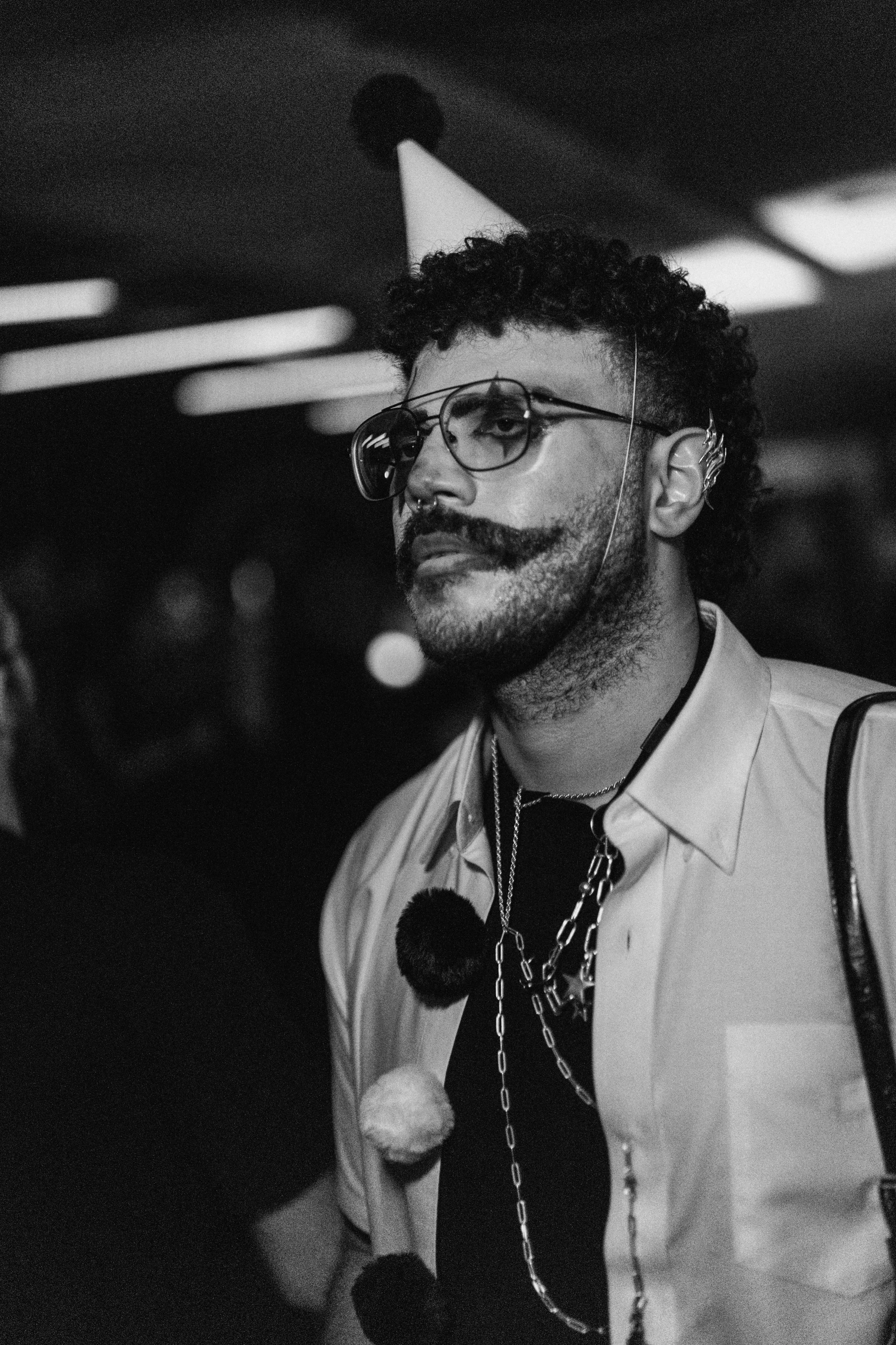 A man with curly hair, glasses, a mustache, and a beard wearing a party hat and chains, at a celebration or party.
