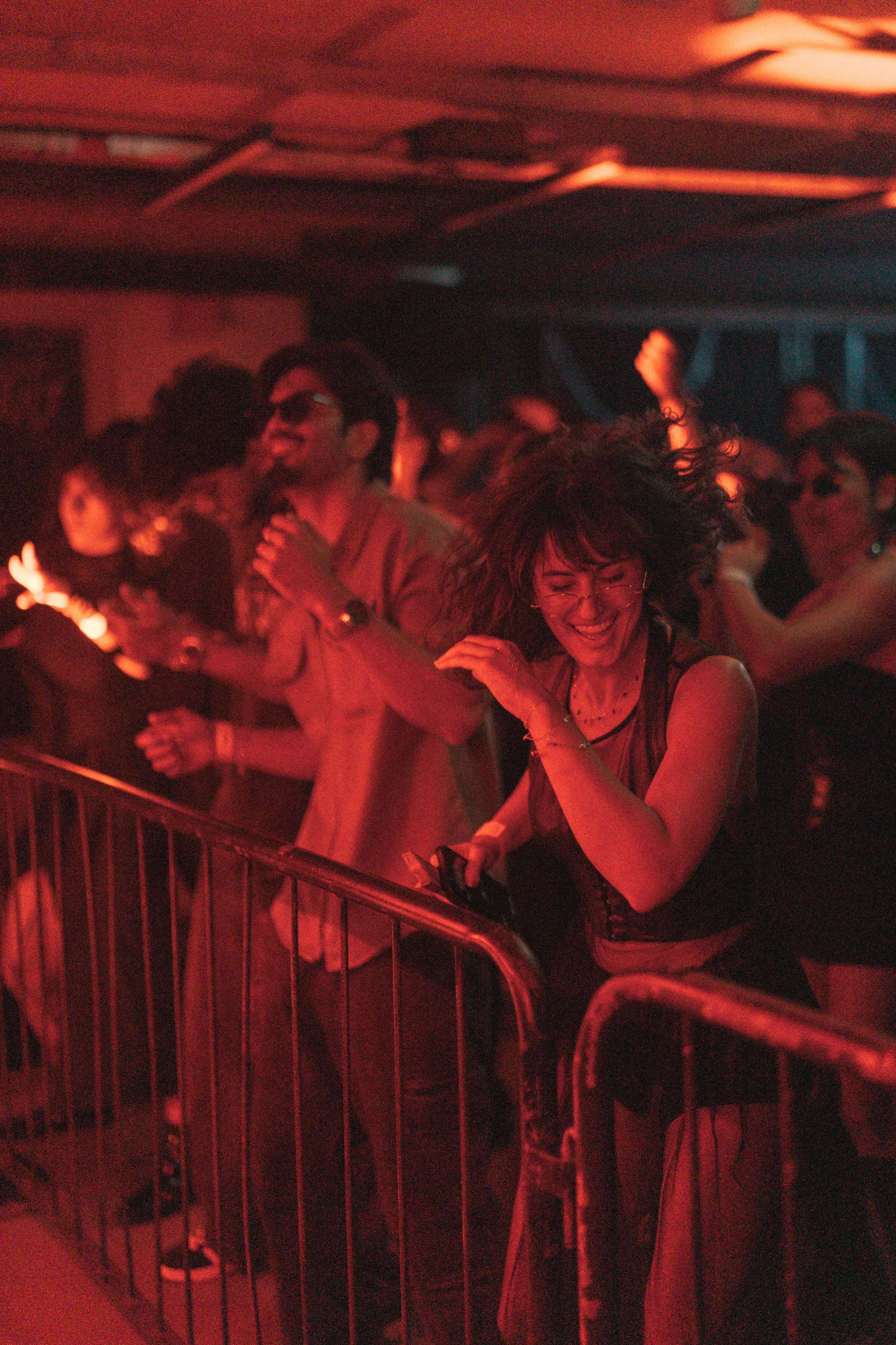 People dancing and enjoying music at a lively indoor concert or nightclub with red lighting.