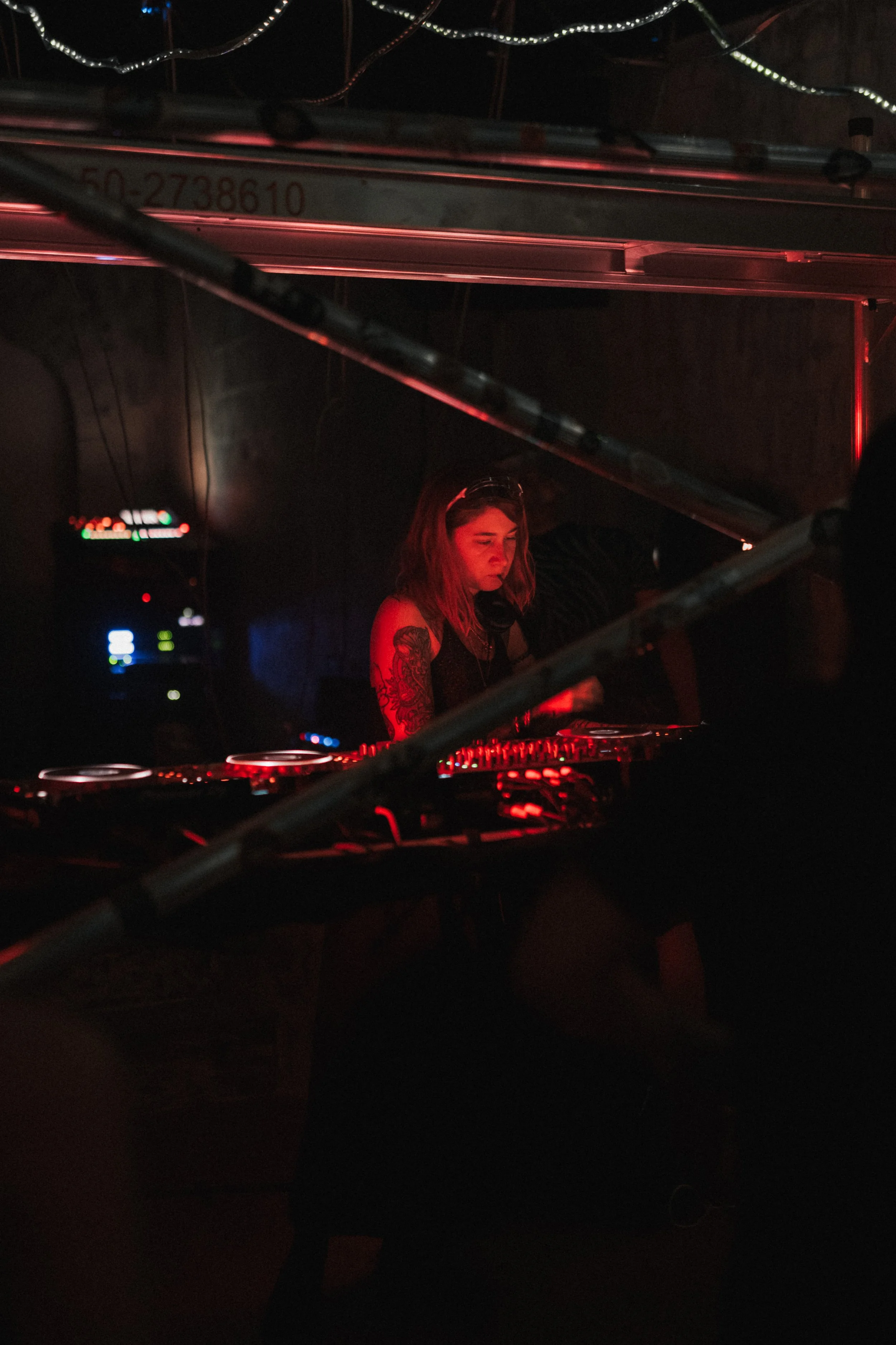 A female DJ in a dark, red-lit nightclub, mixing music on a DJ controller.