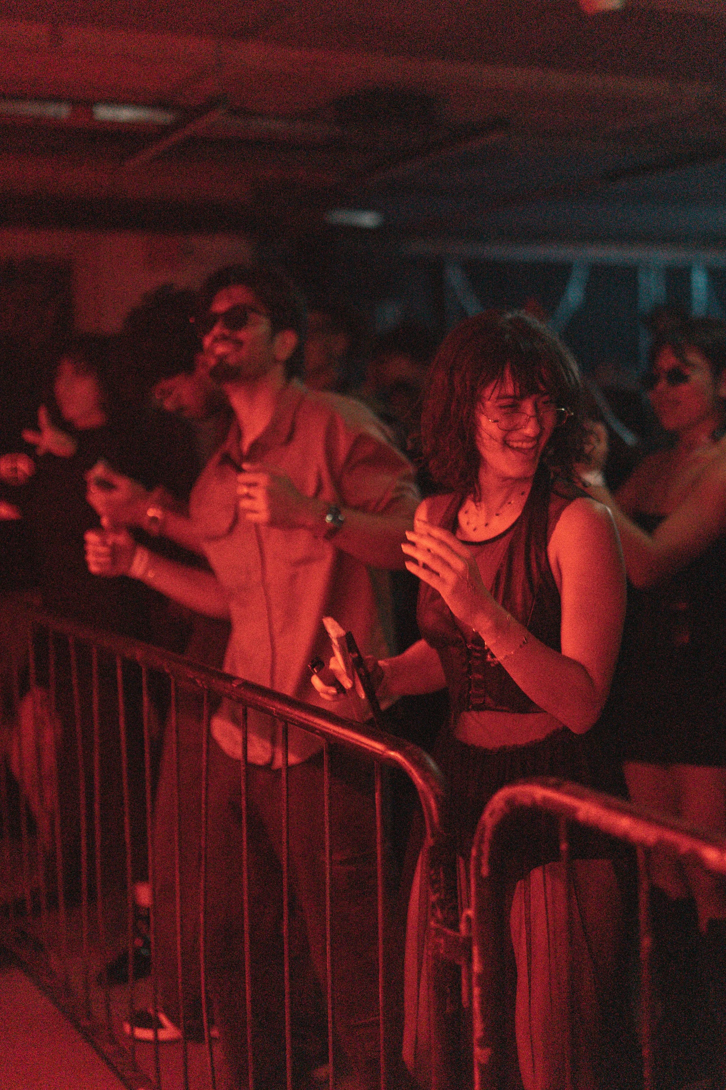 People dancing at a party or concert in a dimly lit venue with red lighting.