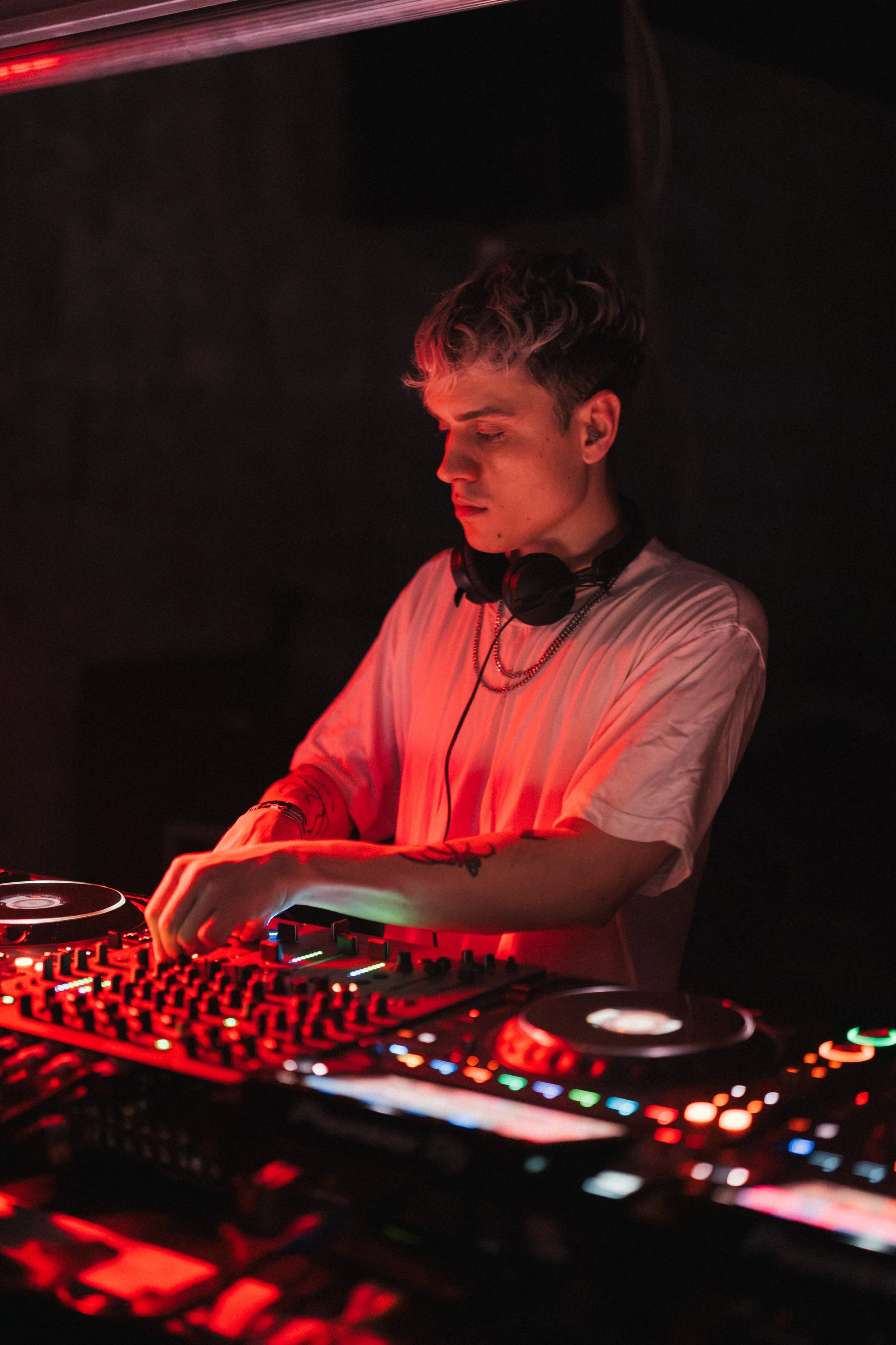 DJ with headphones adjusting controls at a turntable in a dark club with red lighting.