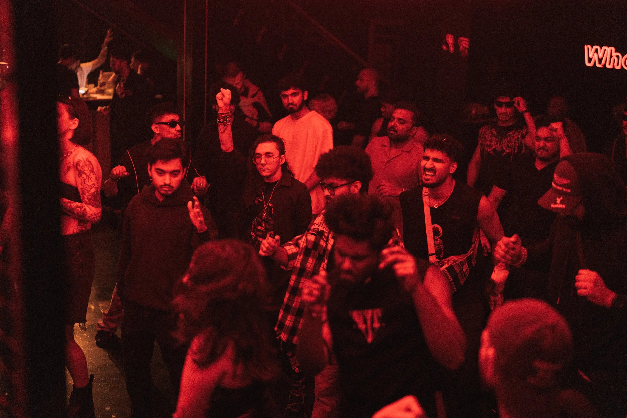 A group of young people dancing and enjoying music in a dimly lit nightclub with red lighting.