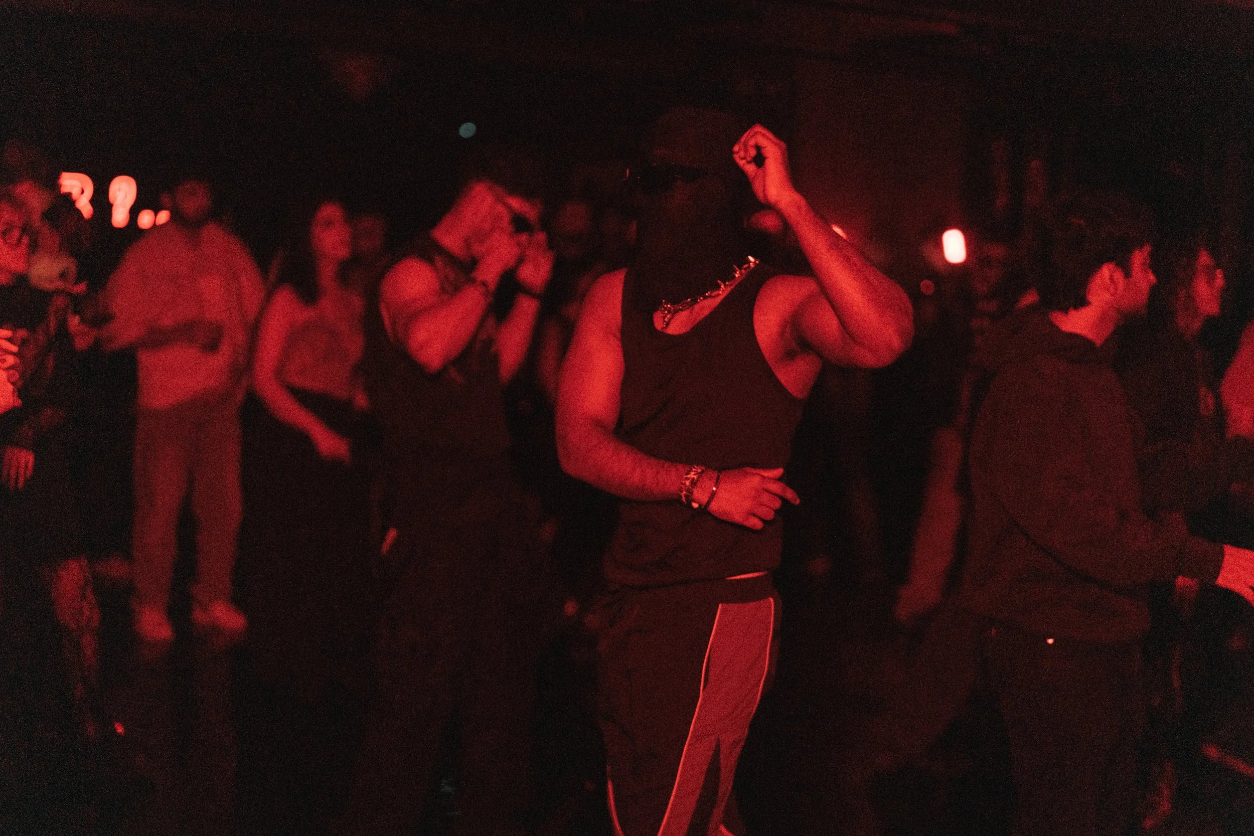 A crowd of people dancing and enjoying music in a dark, red-lit venue.
