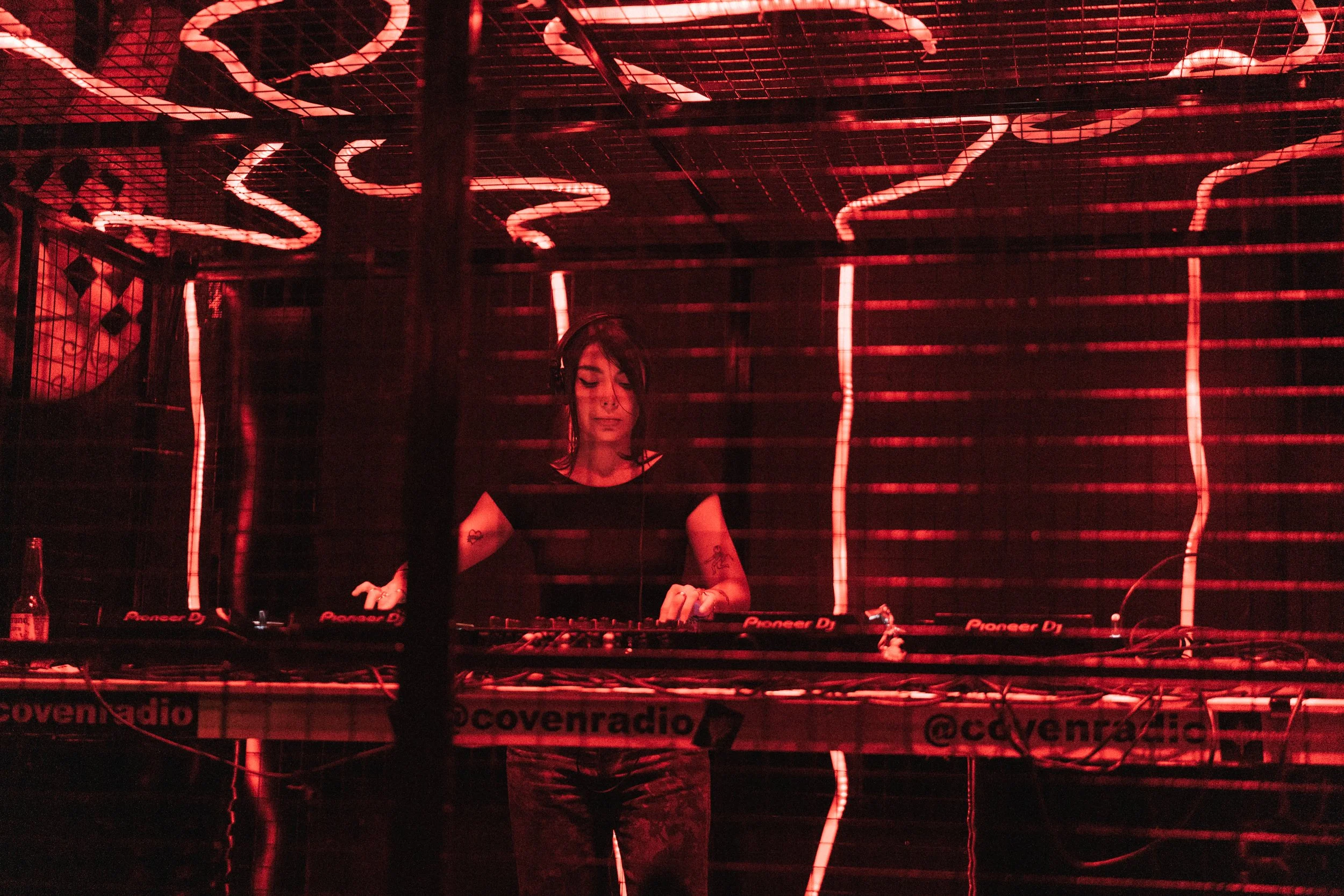 Female DJ performing behind a DJ booth with red neon lighting