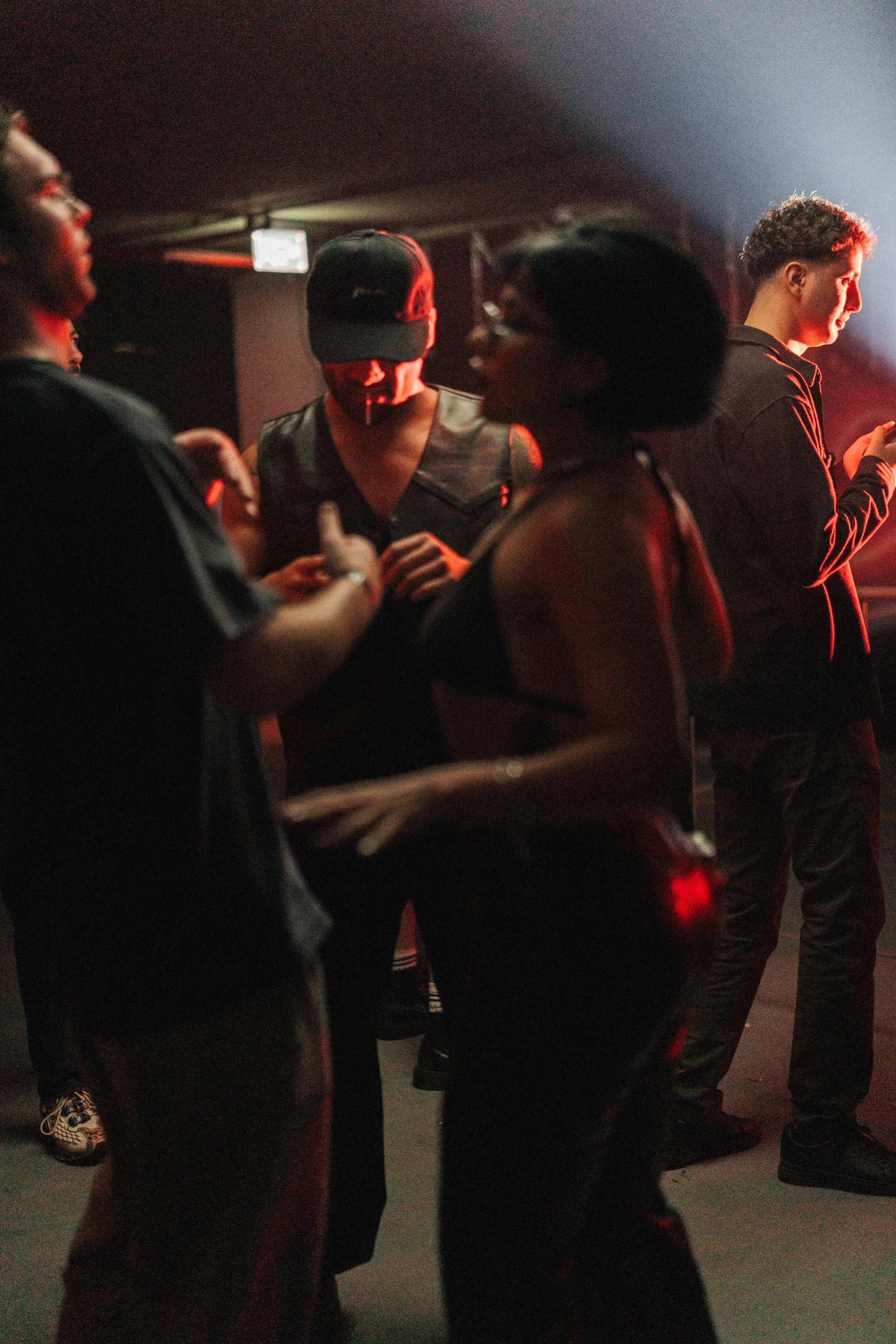 People socializing in a dimly lit nightclub, illuminated by red and white lights, with some using their phones.