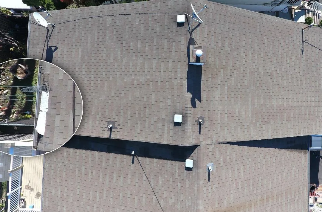 Top-down view of a house roof with satellite dishes, vents, and cables, showing the roof's asphalt shingles and surrounding neighborhood.
