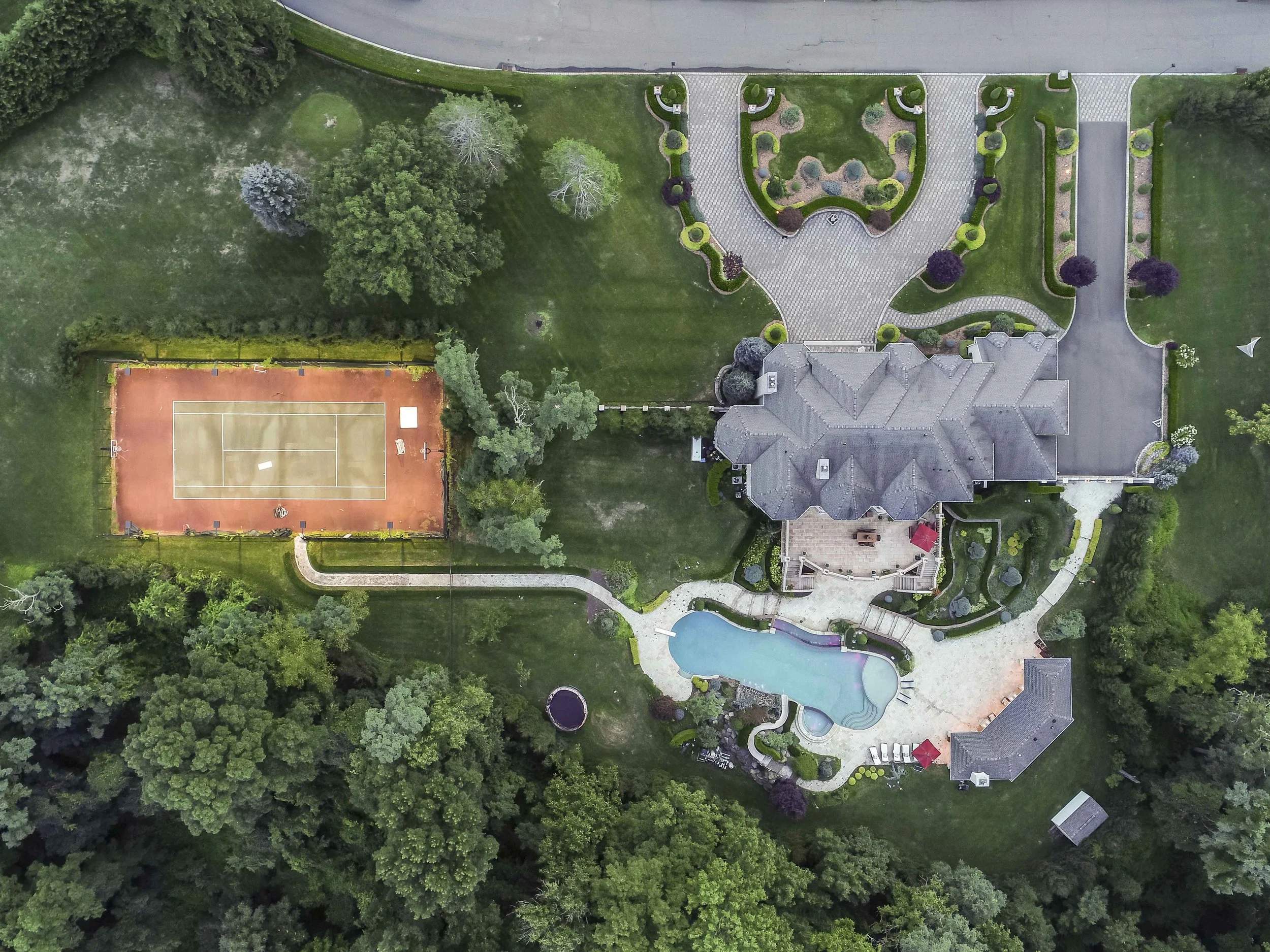 Aerial view of a large estate with a house, swimming pool, tennis court, and garden.