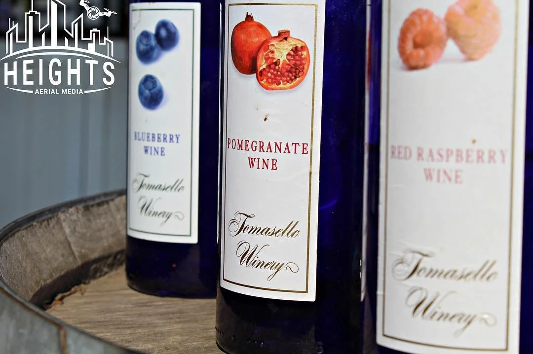 Three bottles of wine labeled blueberry wine, pomegranate wine, and red raspberry wine on a wooden tray.
