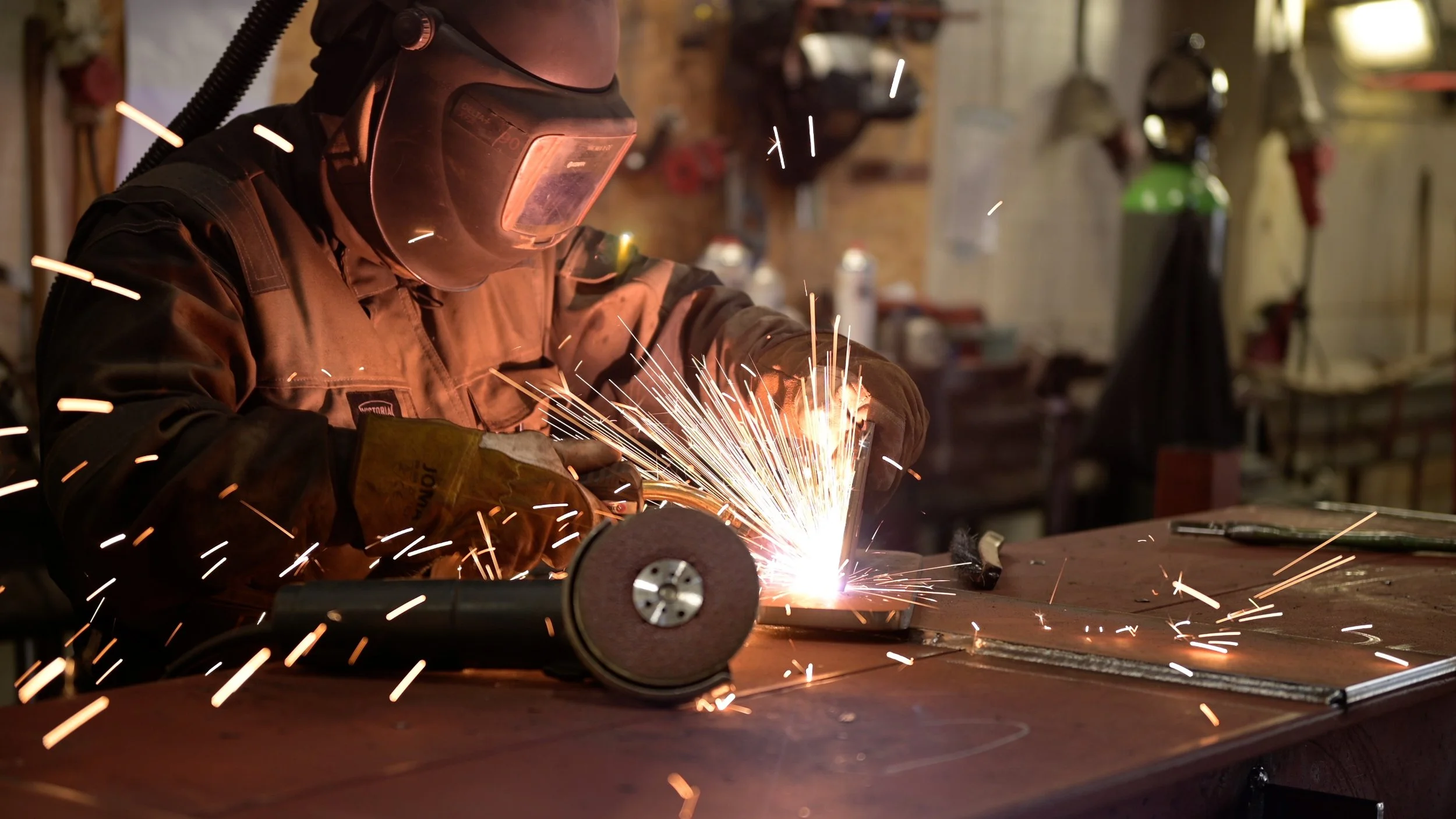 A person welding metal in a workshop, wearing safety goggles and gloves, with sparks flying around.