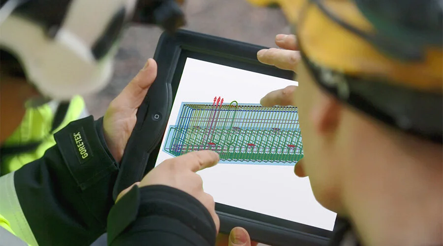 Two people wearing safety gear using a tablet to view a 3D structural diagram.