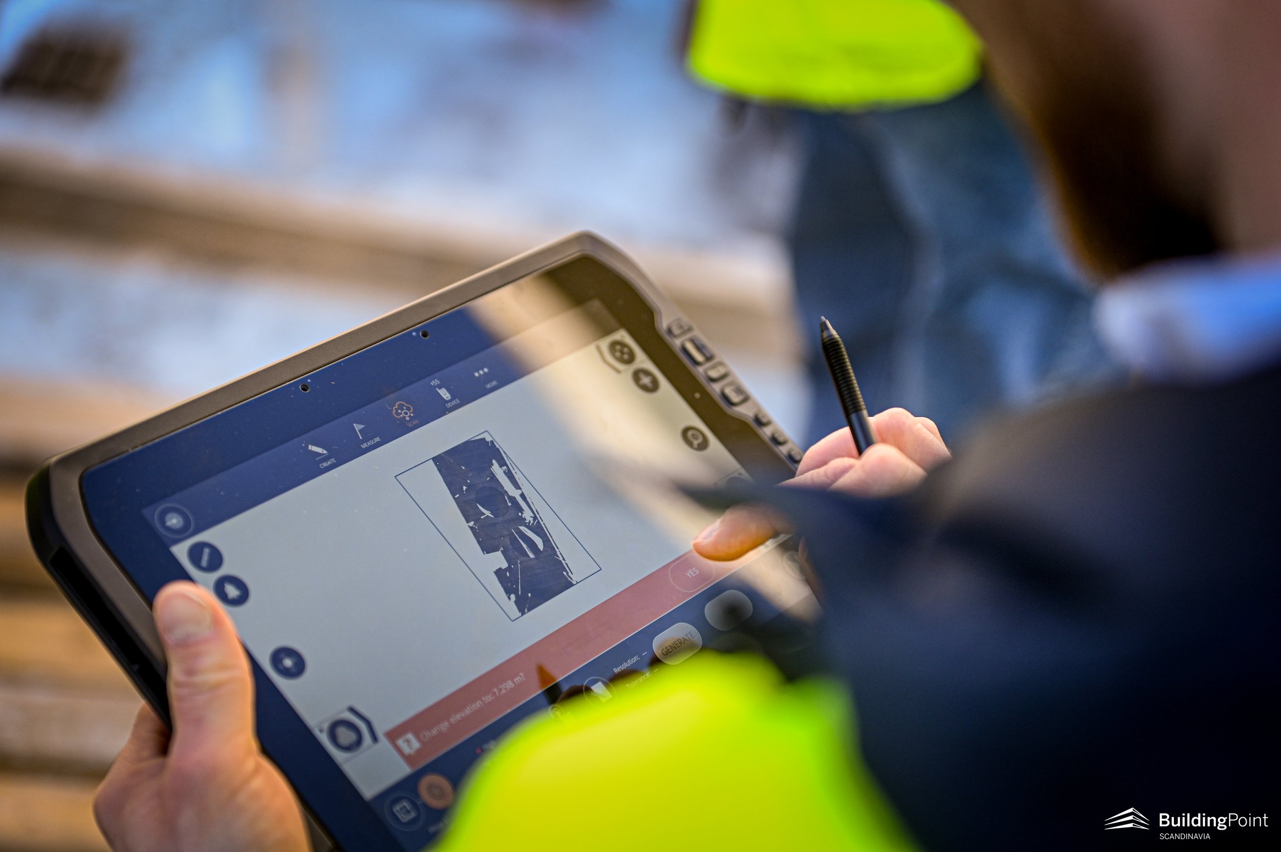 Person using a tablet with a stylus, displaying construction software, and wearing a safety vest on a worksite.