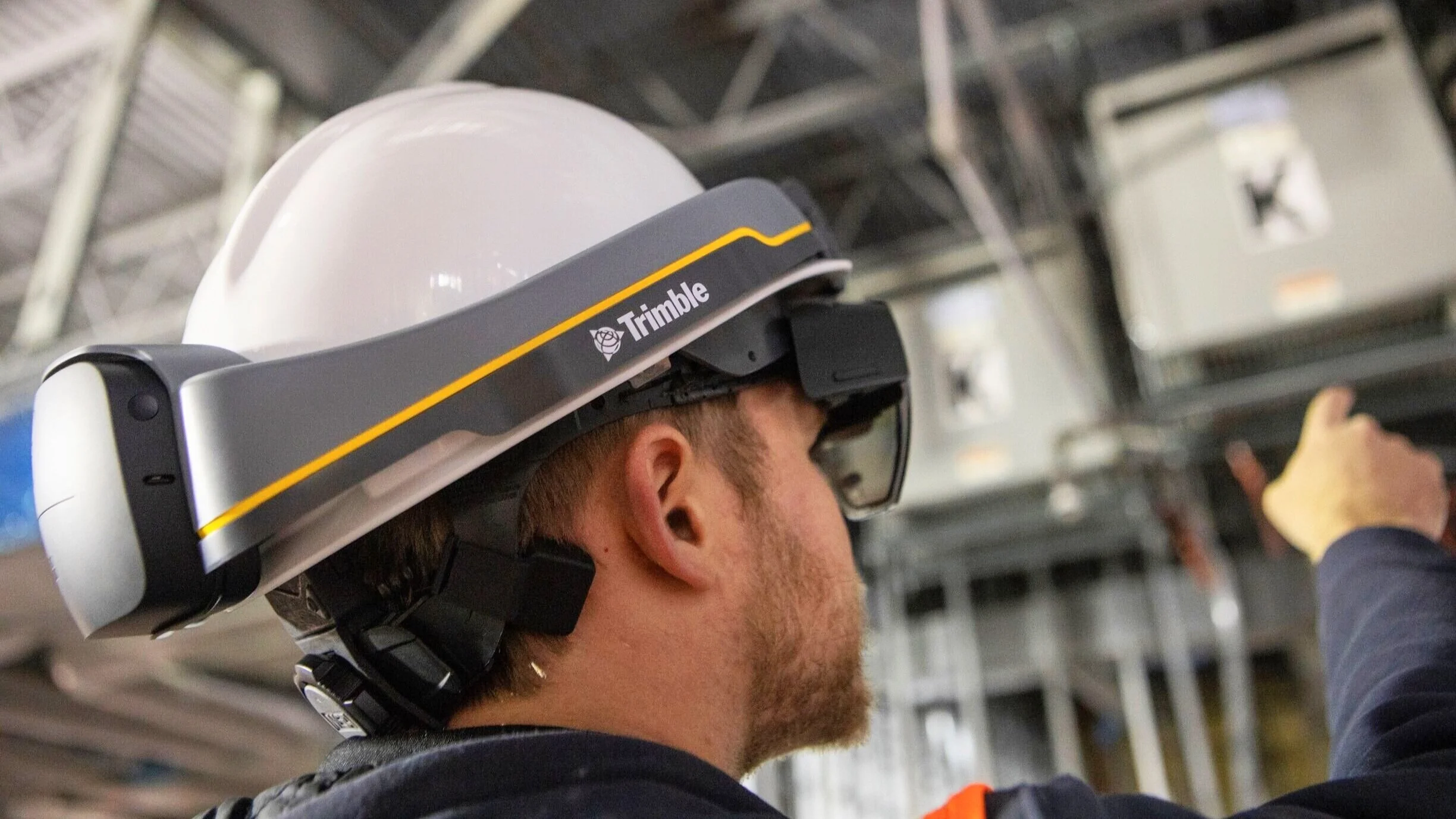 Person wearing a Trimble hard hat with augmented reality headset in a construction setting.
