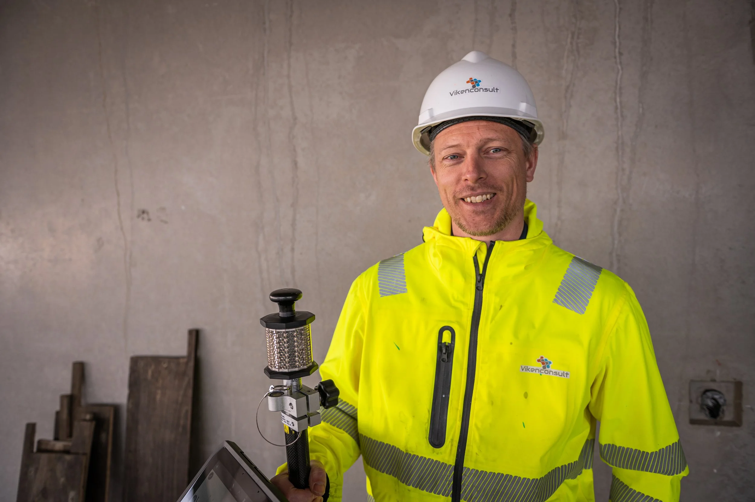 Man in high-visibility jacket and hard hat holding construction equipment.