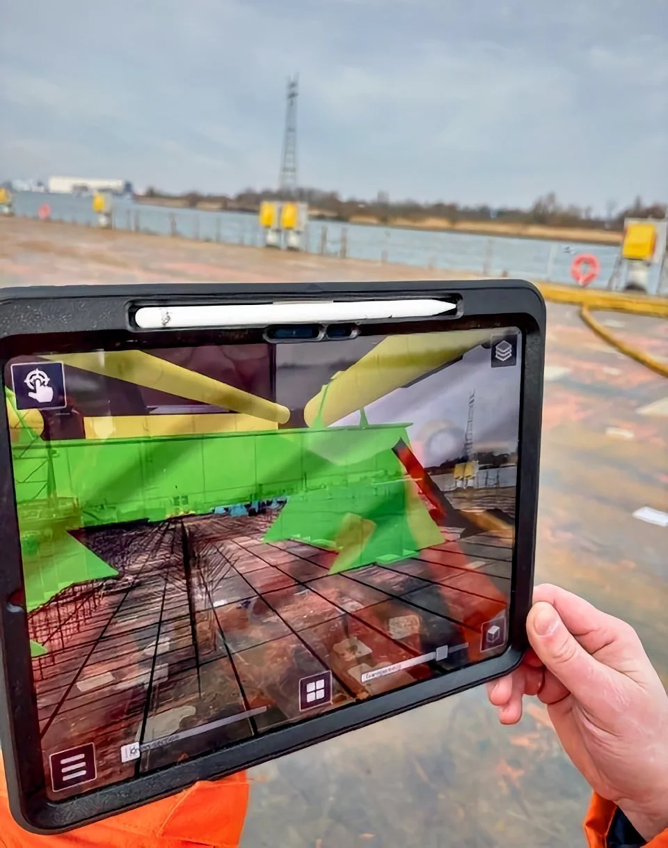 Trimble SiteVision Core - Person holding a tablet with augmented reality overlay on a construction site or industrial area, showing a 3D model of a structure.