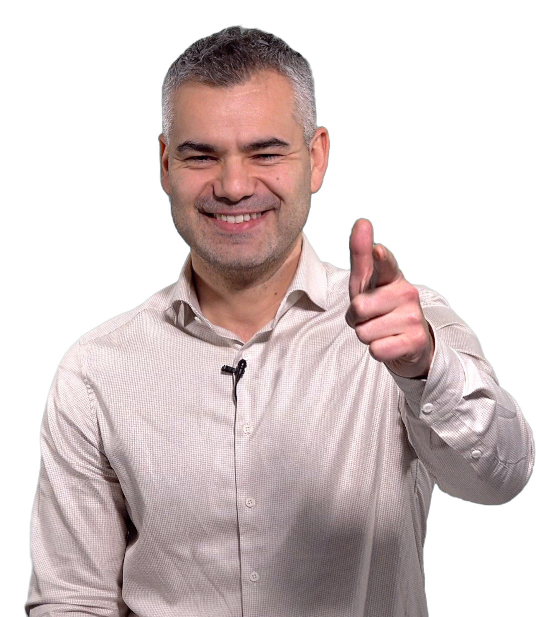 A middle-aged man with short, gray hair smiling and pointing directly at the camera, dressed in a light-colored, collared shirt, with a black microphone clipped on his shirt.