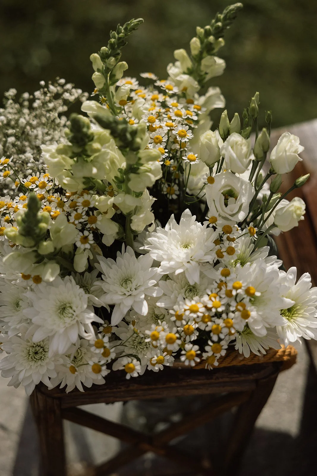 Hvitt blomsterarrangement i kurv med liljer, krysantemum og små hvite blomster.