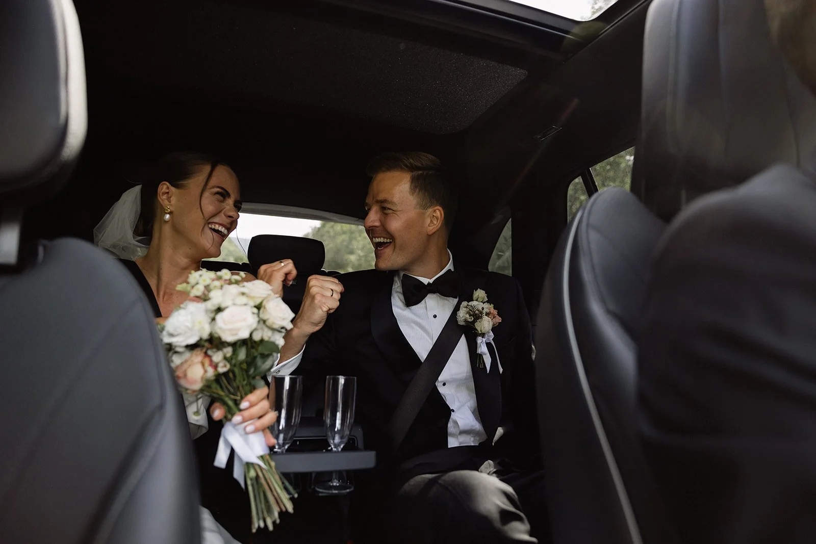 Et brudepar ler og har det gøy i baksetet av en bil, med blomster og champagne.