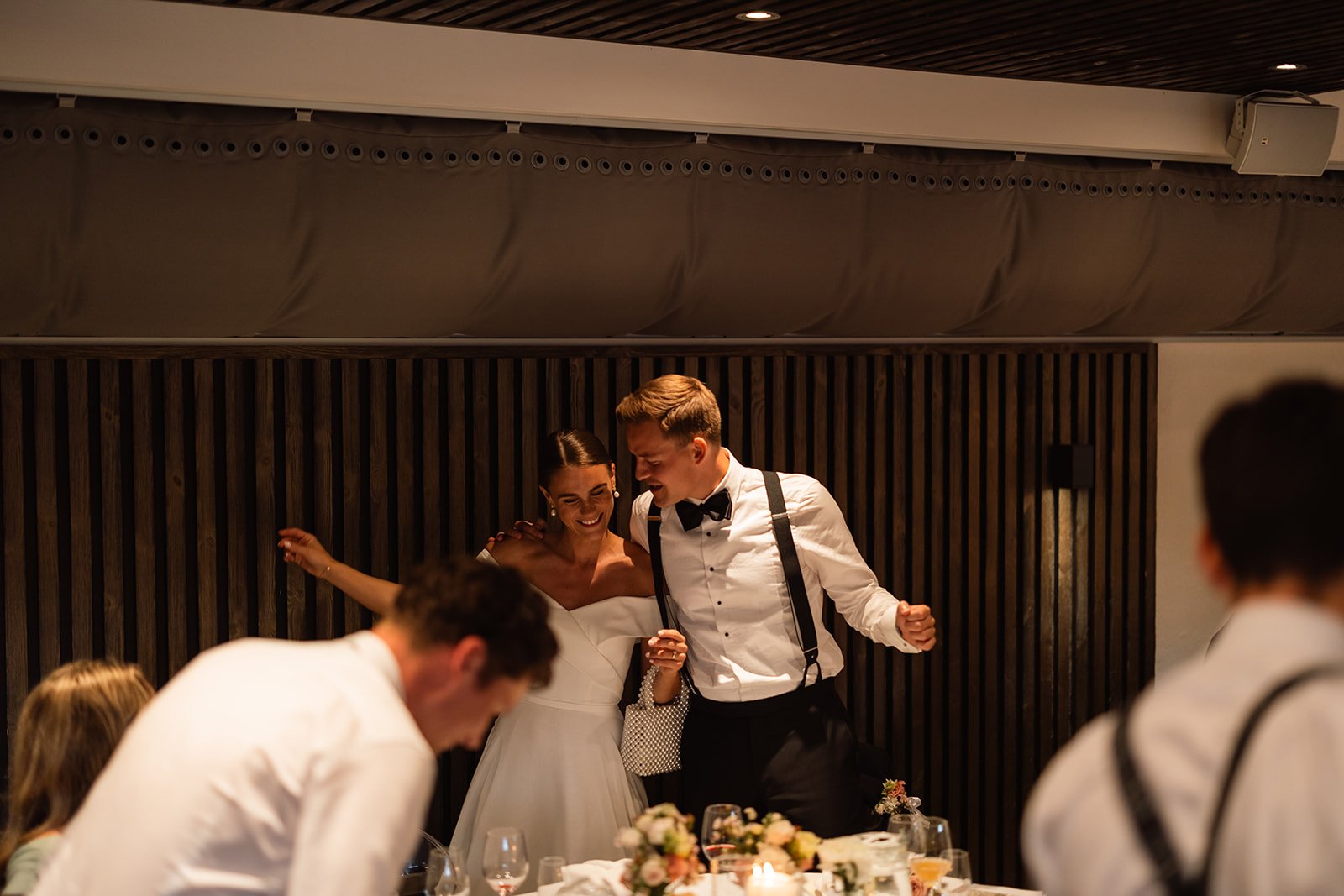 Brudepar som danser på et bryllupsbord, omgitt av gjester.