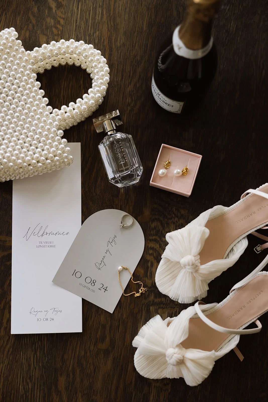Bryllupsdetaljer inkludert perlekjede, parfyme, champagne, smykker, invitasjoner, brudekjole og sko.
