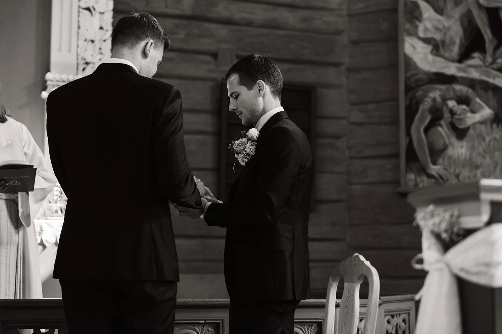 To menn kledd i svarte dresser under et bryllupsseremoni, hvor den ene personen holder den andres hender.