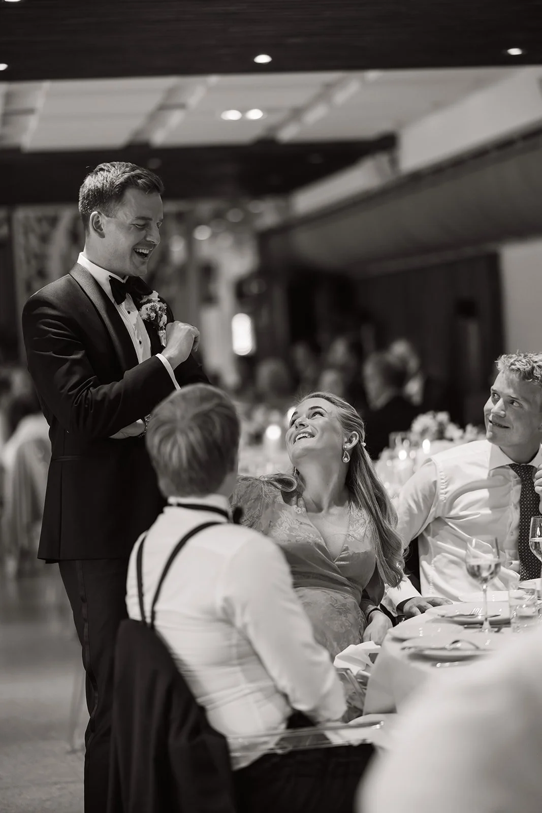 Brude og gjester i bryllupsmiddag, med en mann i dress som holder tale.